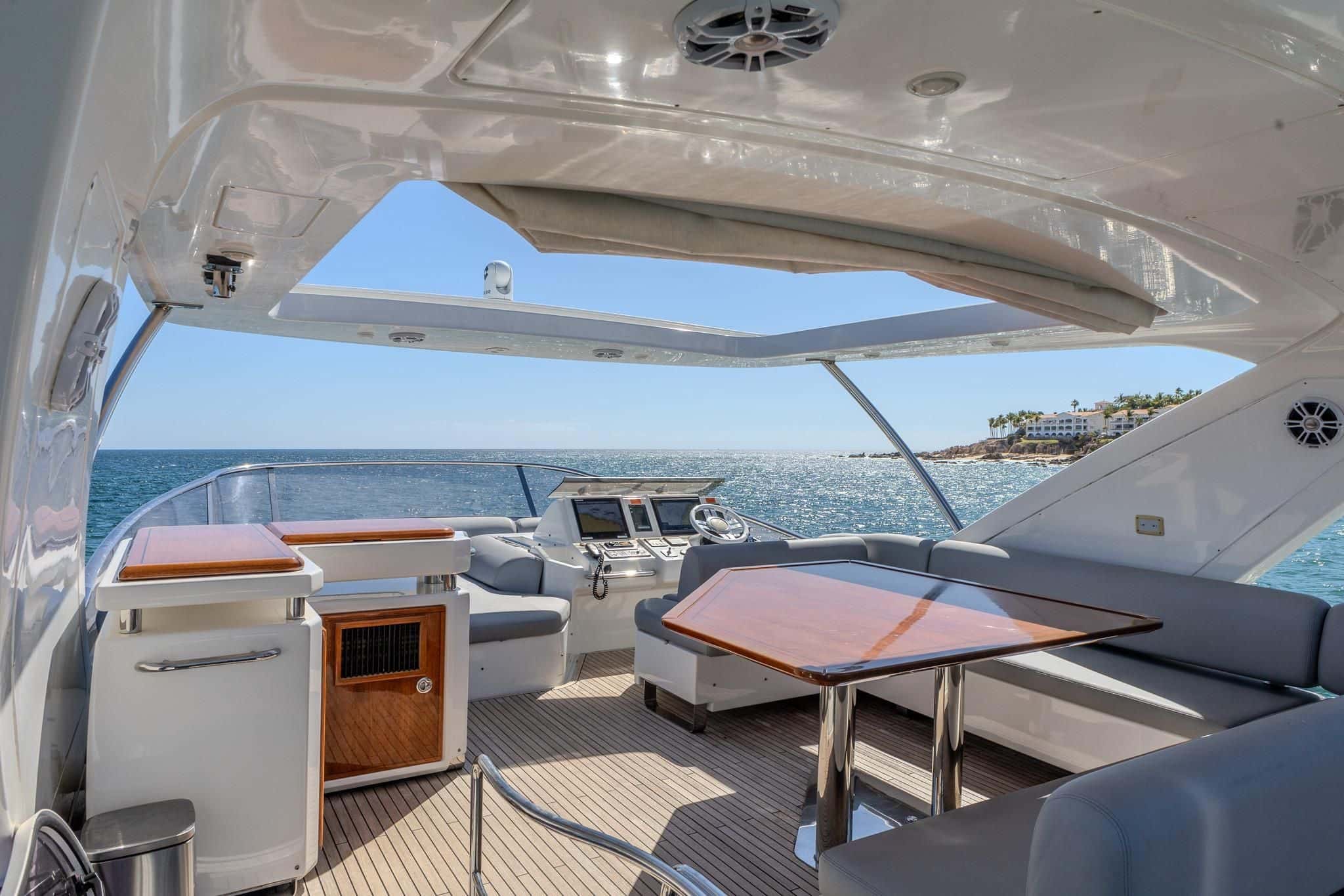 Flybridge under the hardtop with a wooden dining table, grey bench seating and the upper helm forward