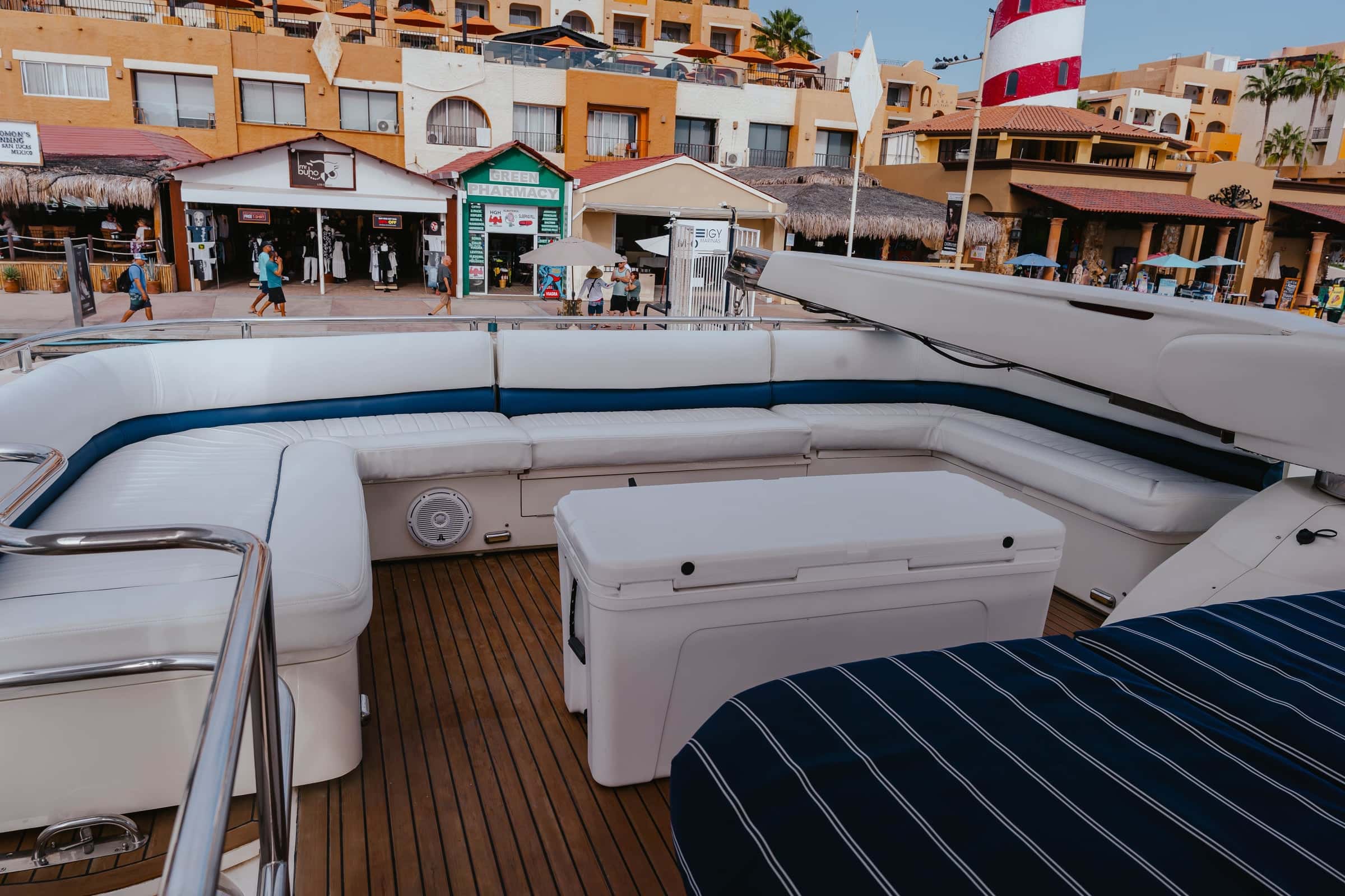 Aft end of the flybridge with wraparound white seating and striped navy sunpads, the Cabo San Lucas waterfront behind