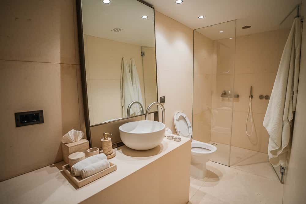 Bathroom with a round white basin on a stone counter, a large mirror, towels and a glass walk-in shower