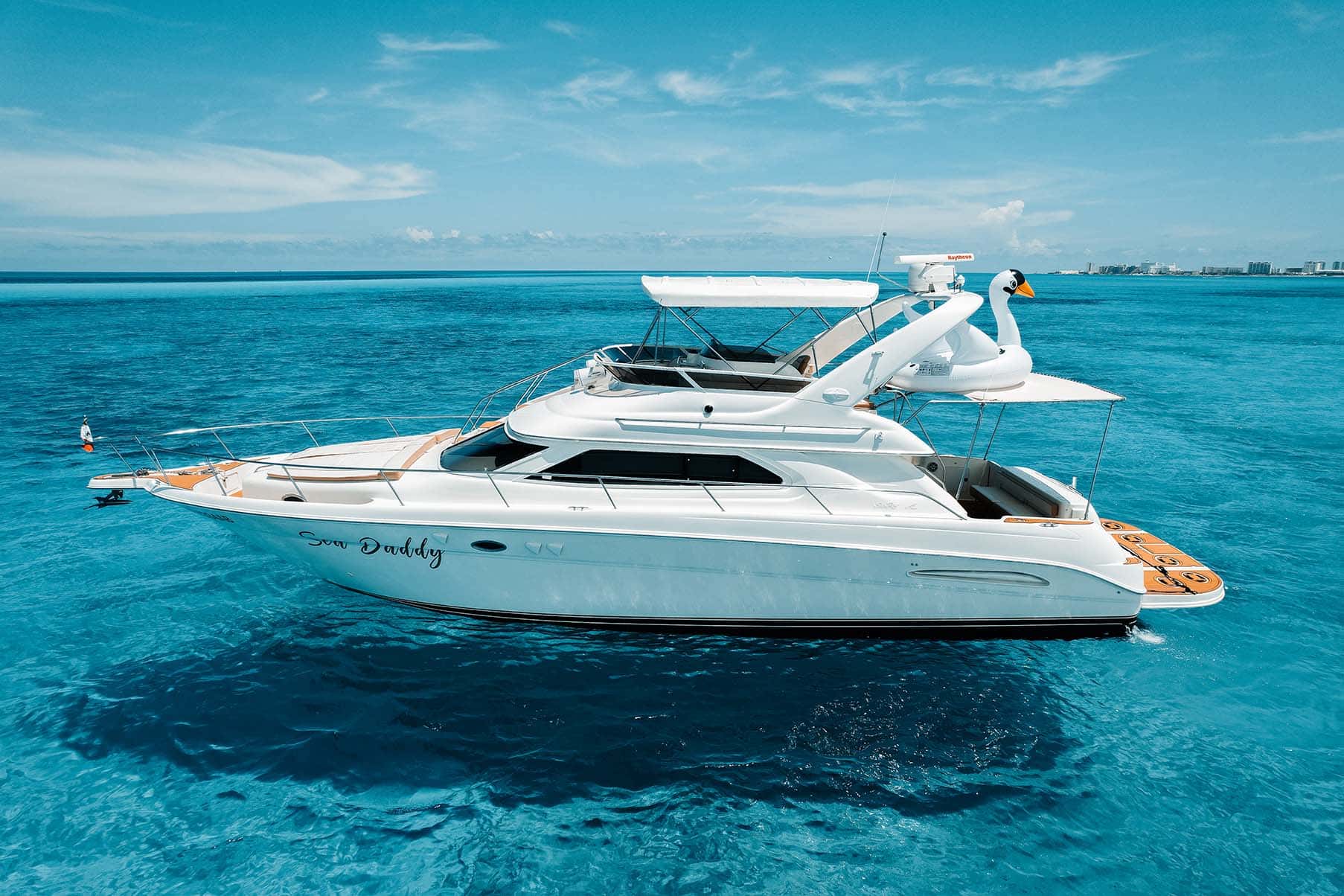 Sea Daddy at anchor seen from the bow quarter, flybridge with bimini and radar arch, Cancun hotel zone behind