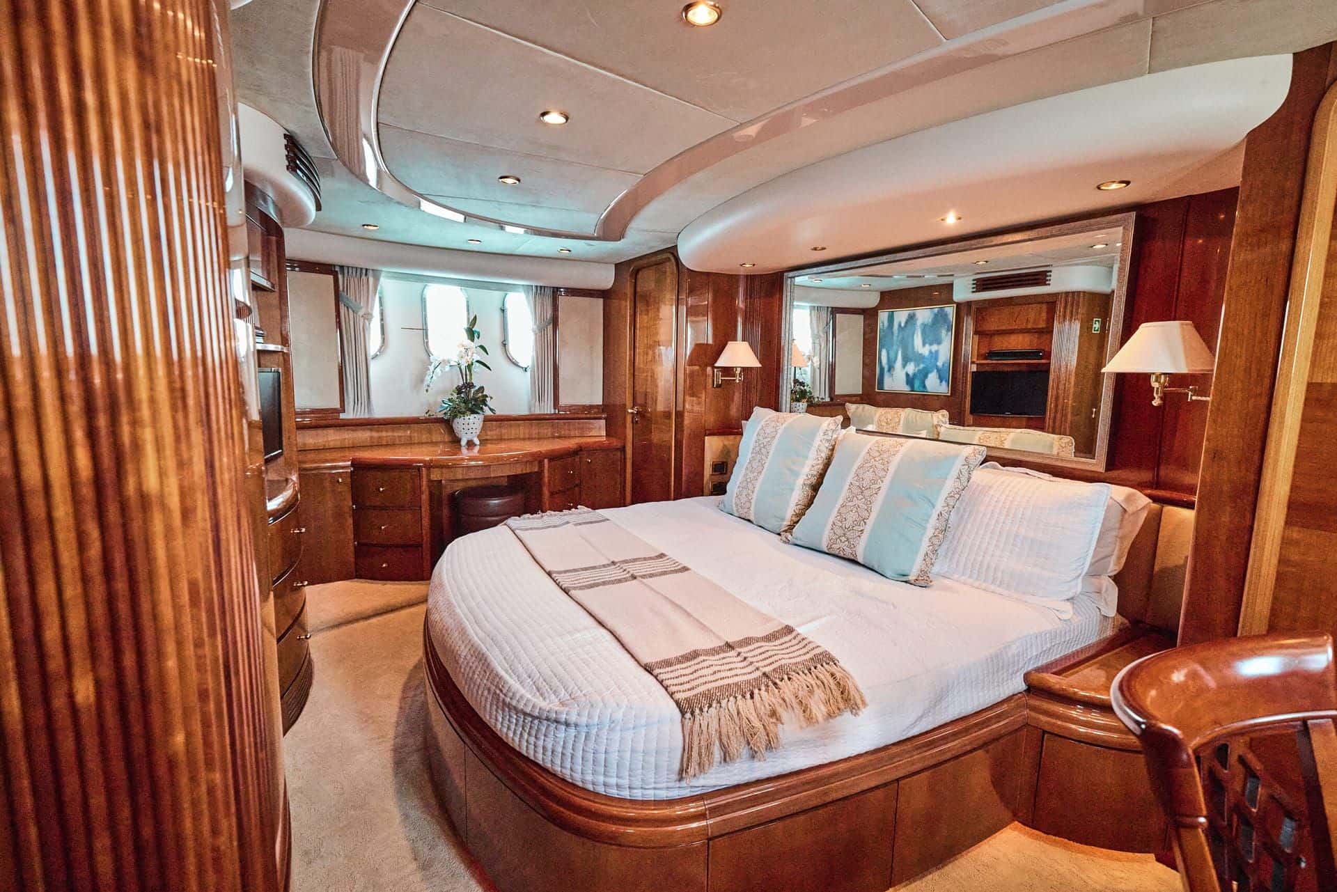Master cabin with a round bed and striped throw, wood panelling, a vanity and oval hull windows