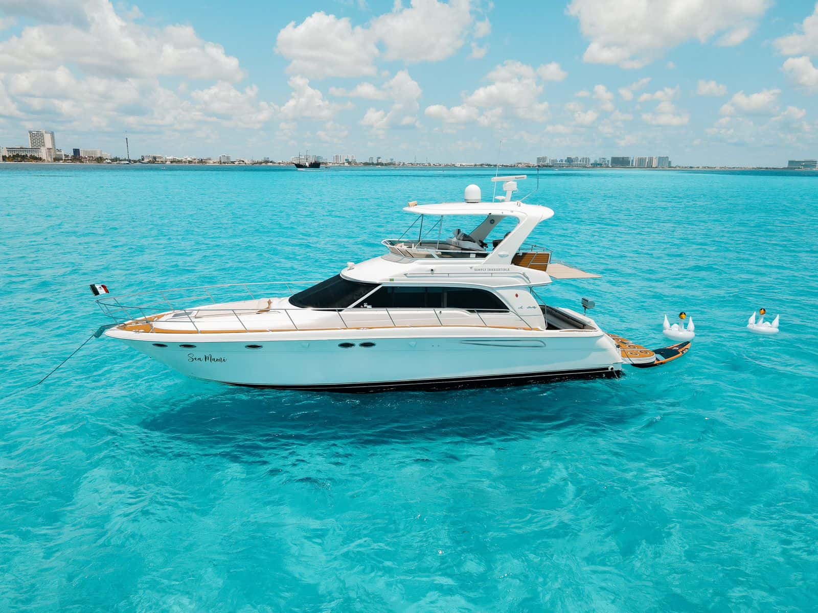 Sea Mami at anchor, full side profile with the flybridge and hardtop and the Cancun hotel zone behind