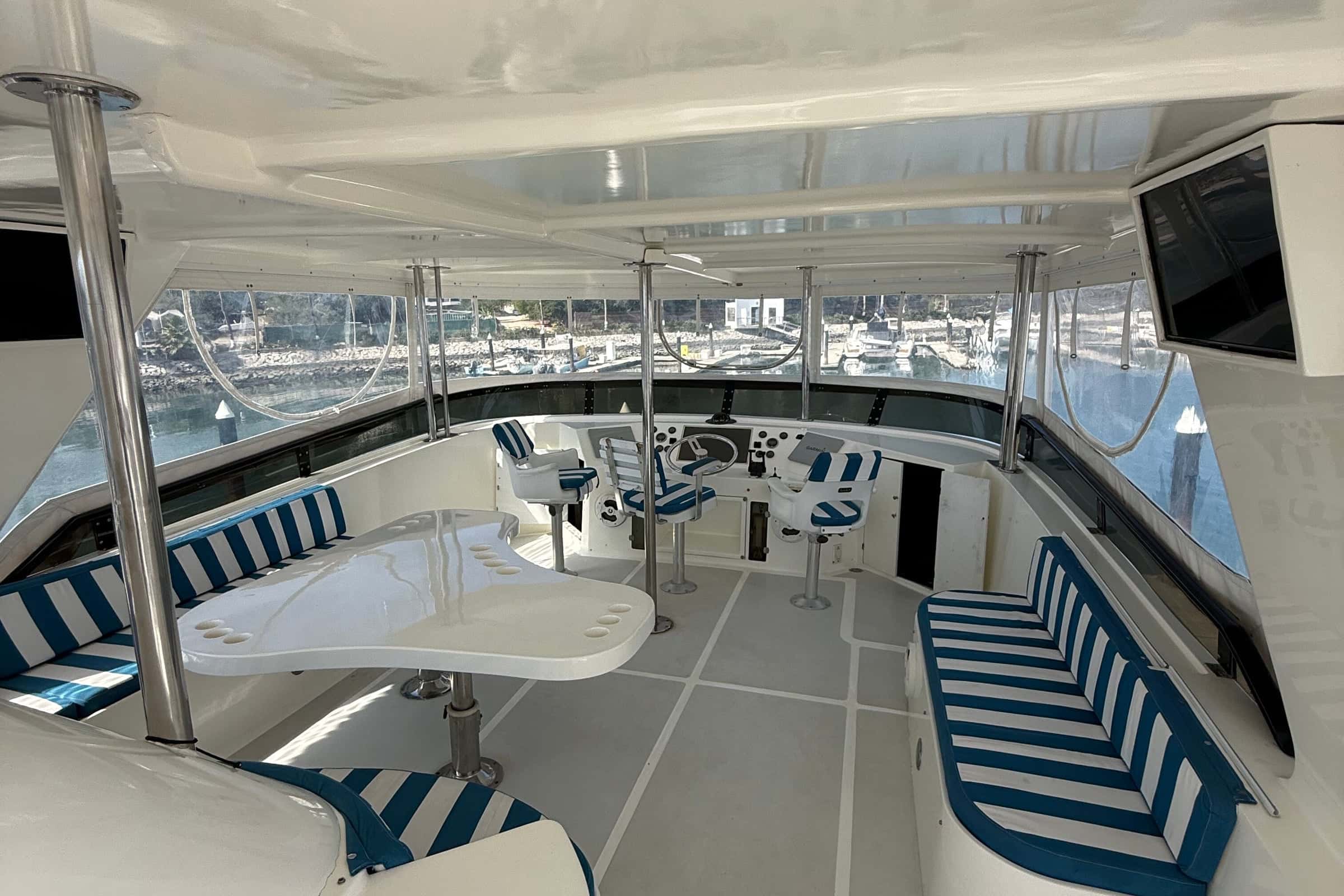 Flybridge with blue and white striped settees around white tables under the hardtop, the helm beside them