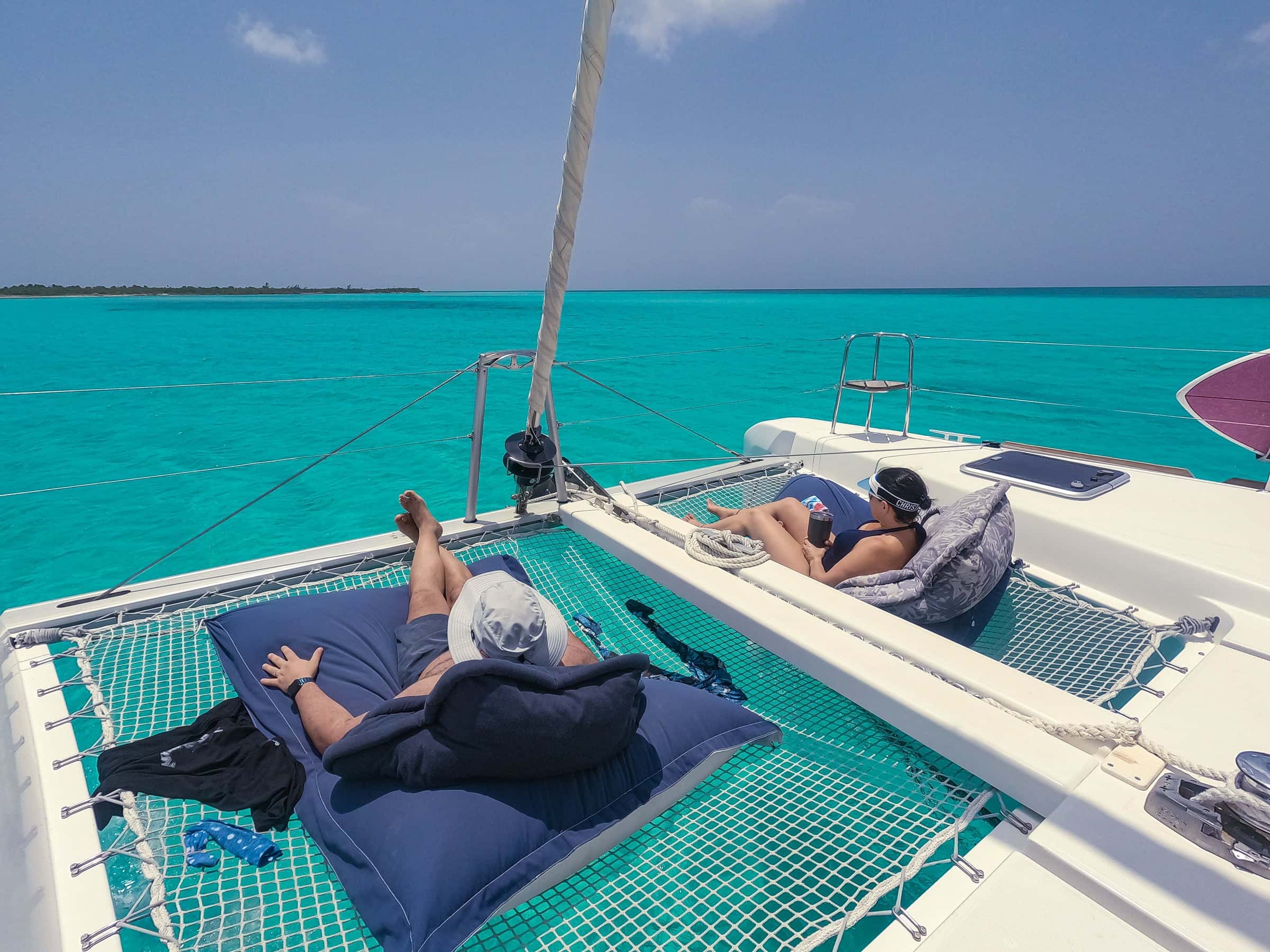 Guests lying on cushions on the trampoline nets between the bows, turquoise water ahead
