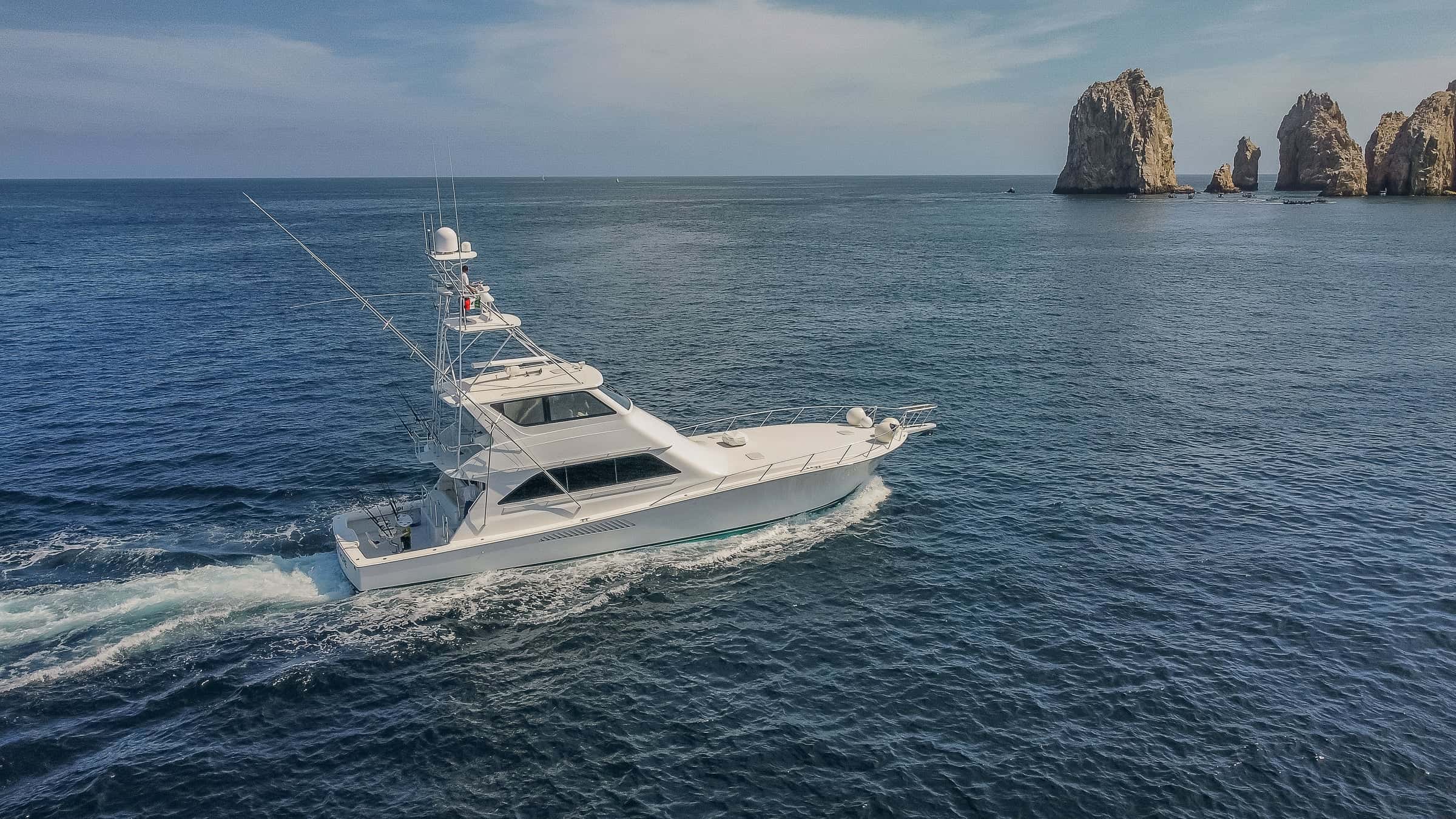 Les Is More, a white sportfishing yacht with a tuna tower, under way with rock stacks rising from the sea behind