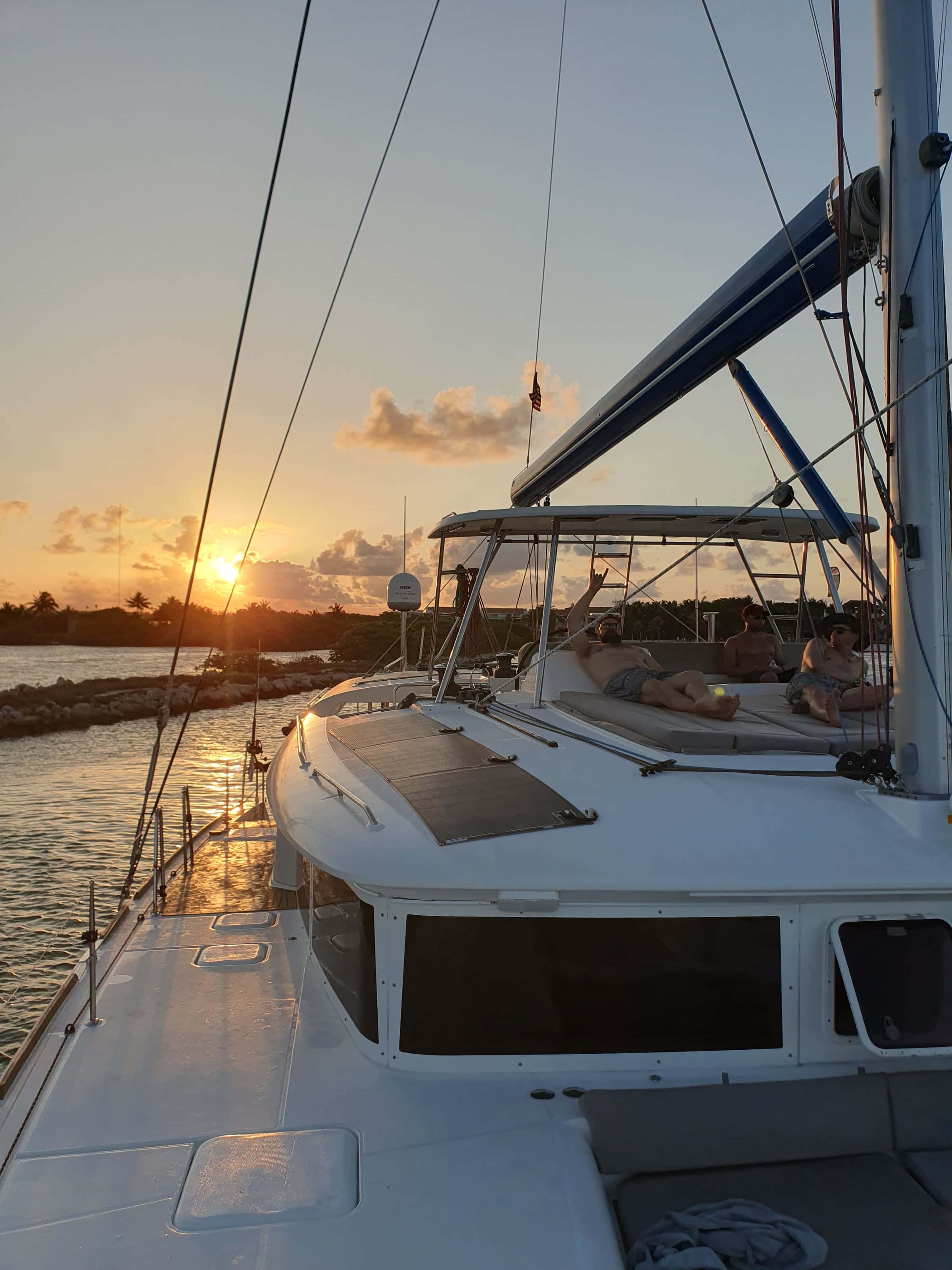 Guests lounging on the flybridge at sunset as the catamaran leaves the marina