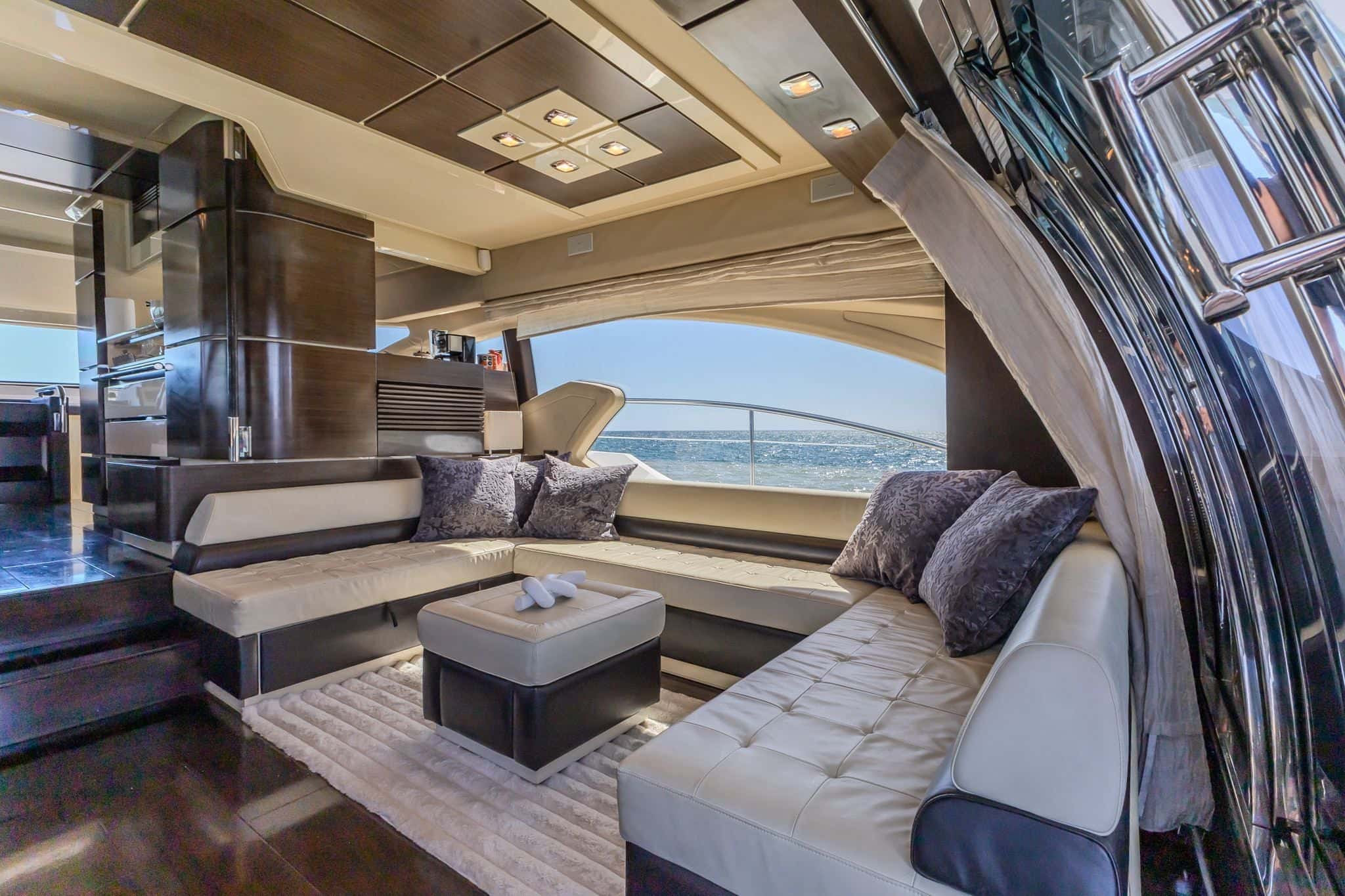 Saloon with a cream leather U-shaped sofa around an ottoman, the sea through the long side windows