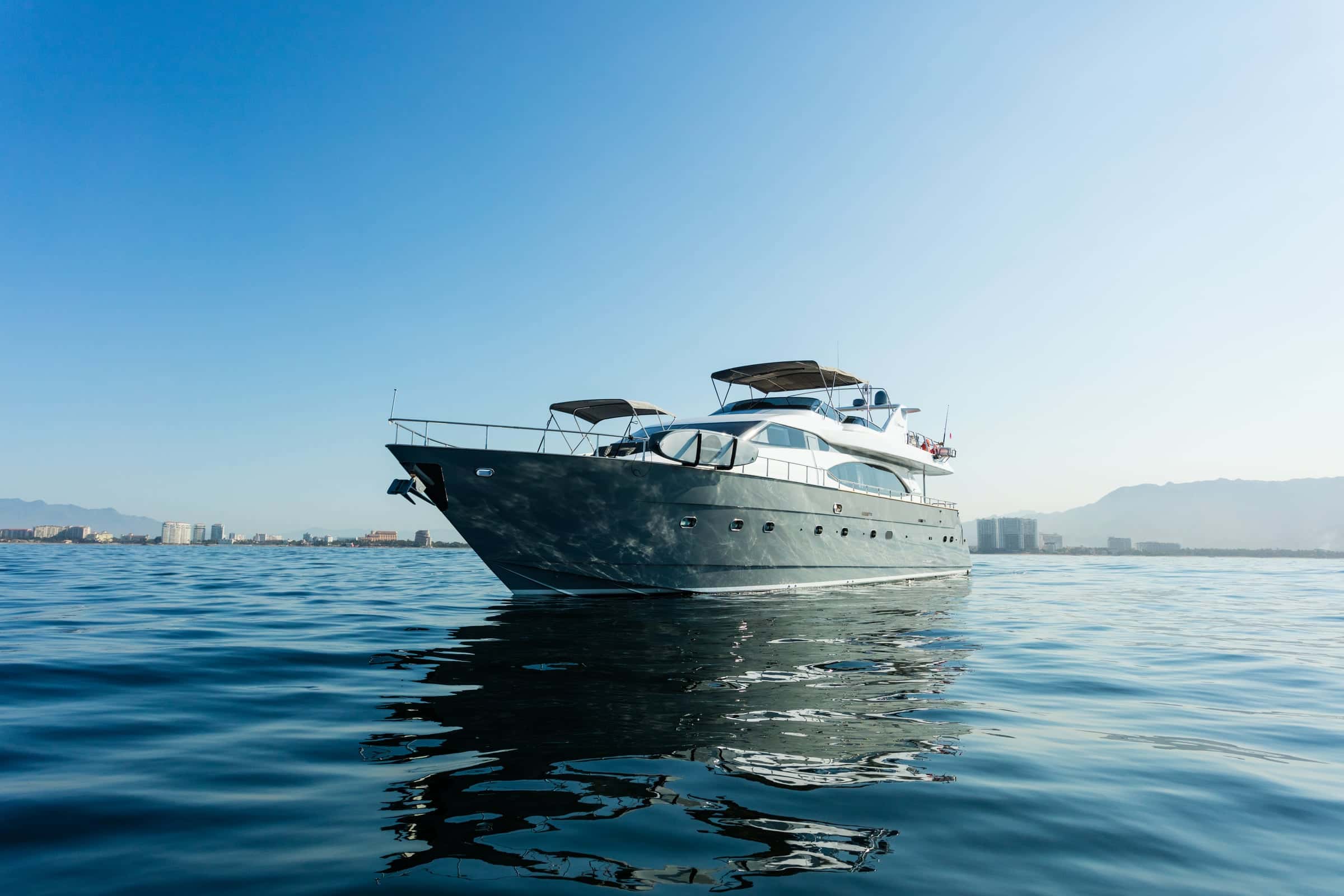 Don Moi, a grey-hulled Azimut flybridge yacht, at anchor on calm water with the shore and hills behind