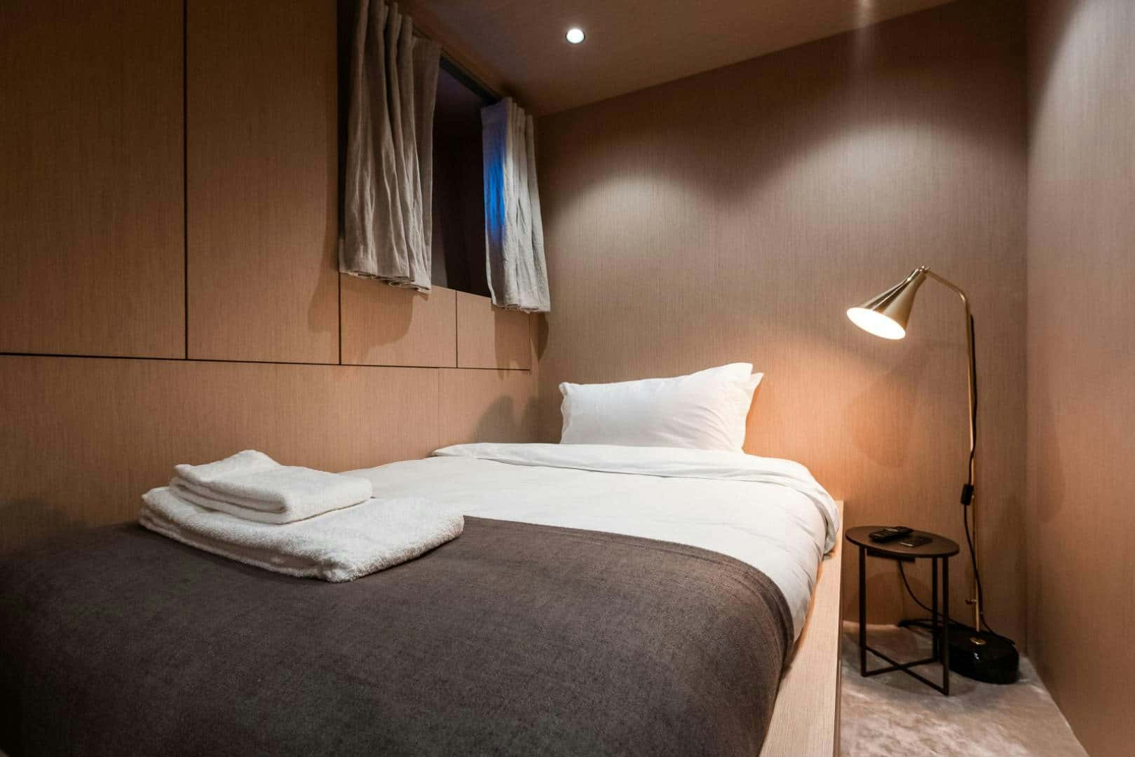 Cabin with a made-up bed, towels folded on it and a brass reading lamp