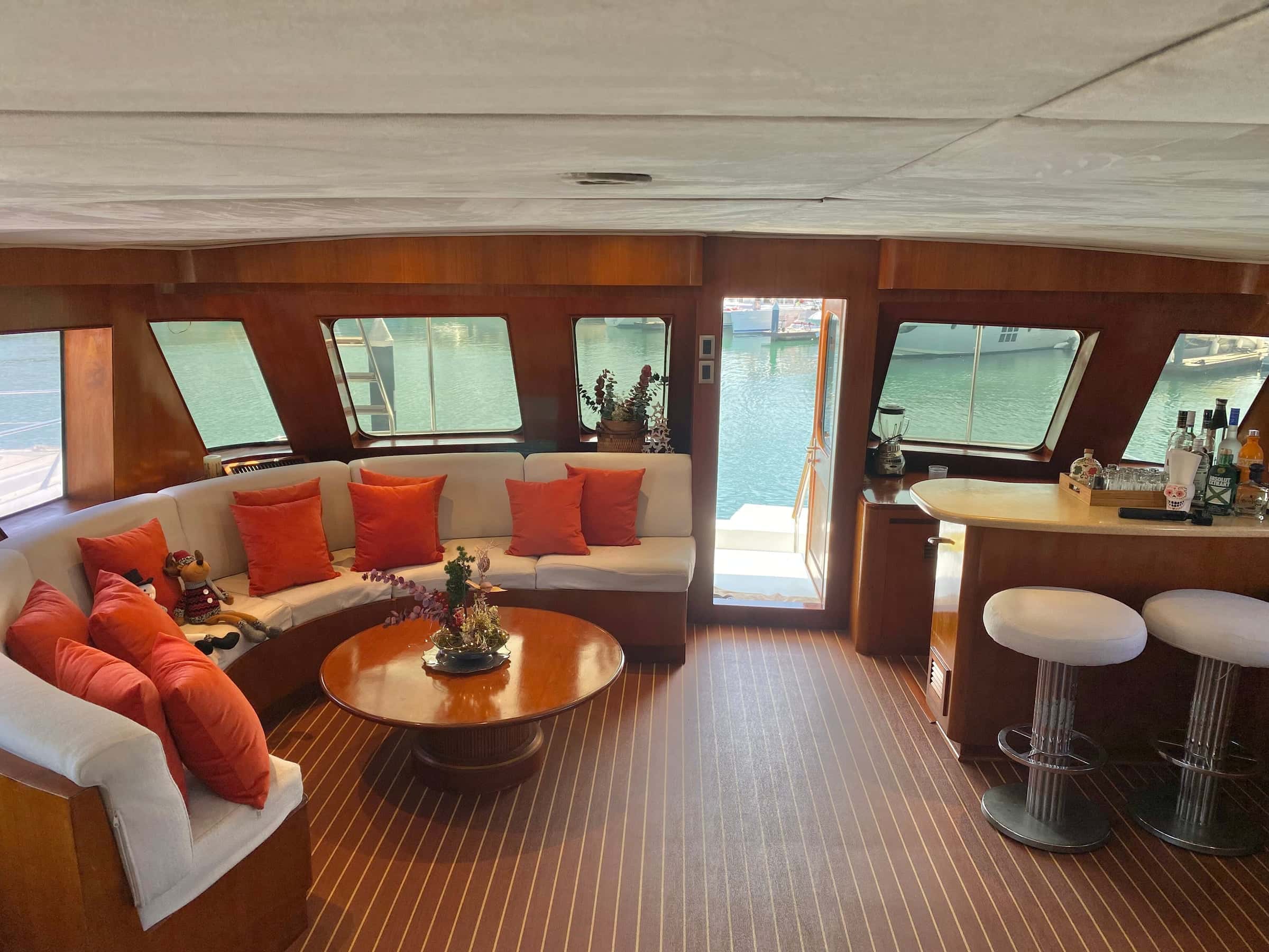 Saloon with a curved sofa and orange cushions around a round table, and a bar with two stools