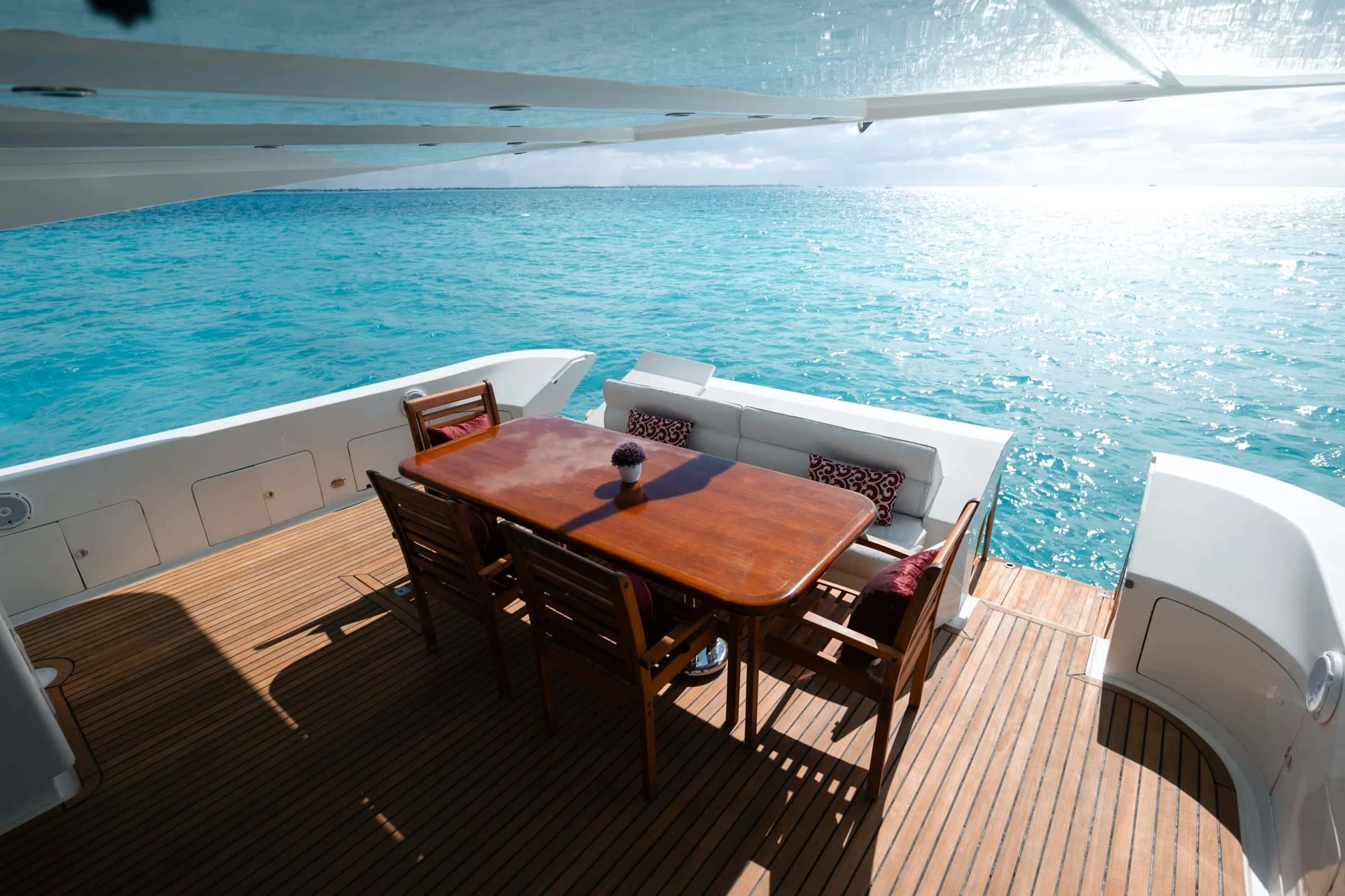 Teak dining table and chairs on the shaded aft deck, with a cushioned bench along the stern