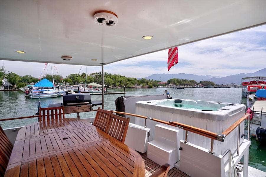 Covered aft deck with a teak dining table and chairs, the hot tub at the stern