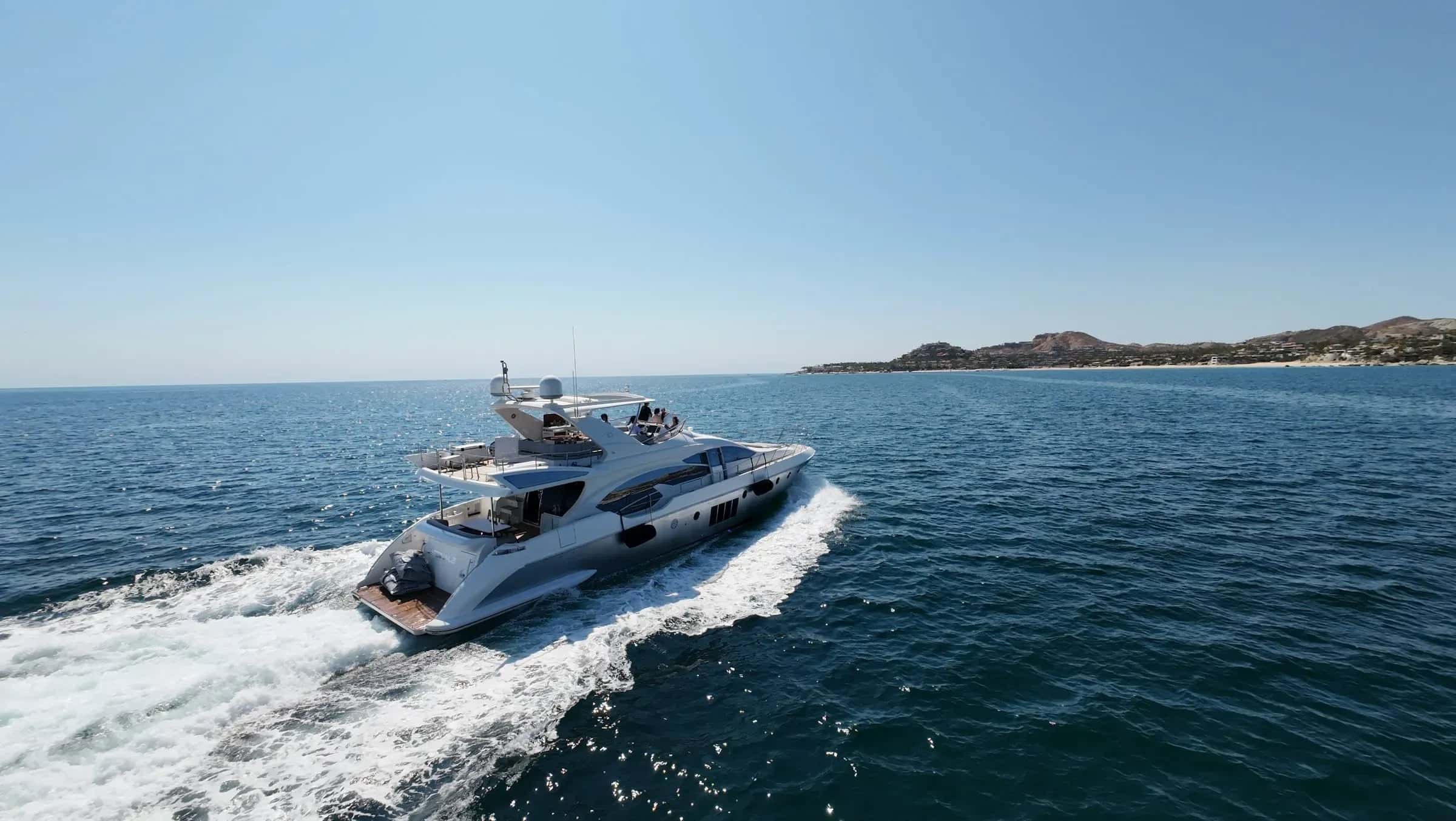 Cardinale running at speed off Los Cabos seen from a drone astern, a white wake behind and the coast beyond
