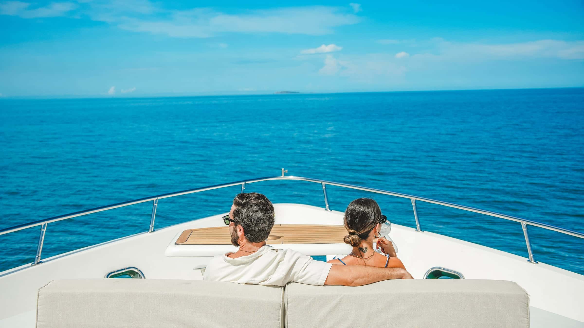 Two guests with a drink sitting on the bow looking at the open sea