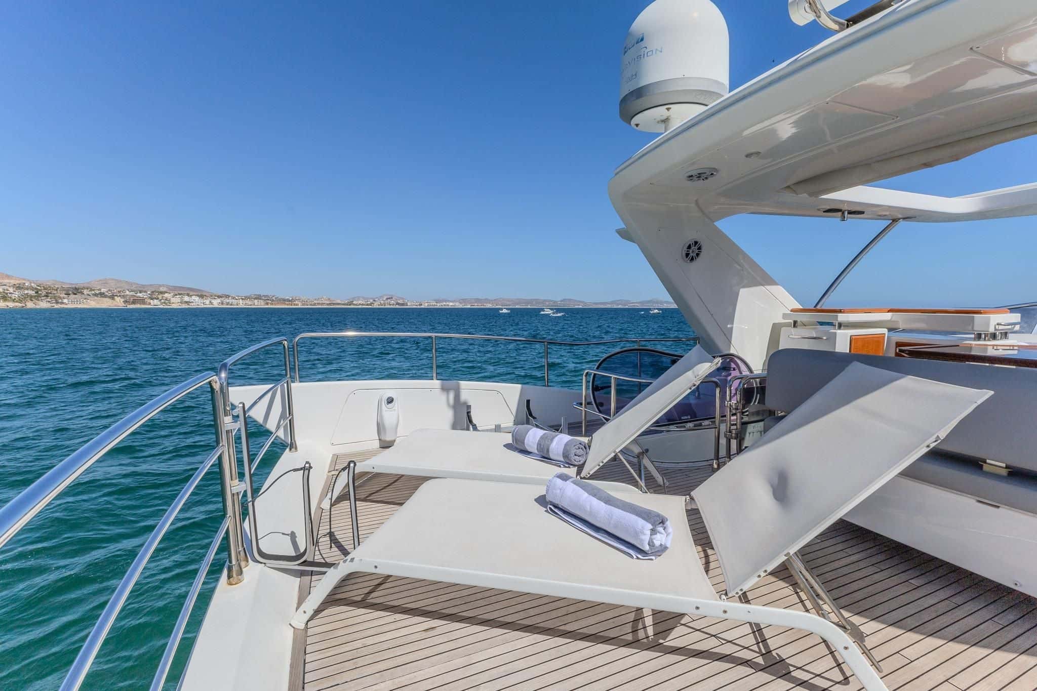Two sun loungers with rolled towels on the teak foredeck, the coast beyond