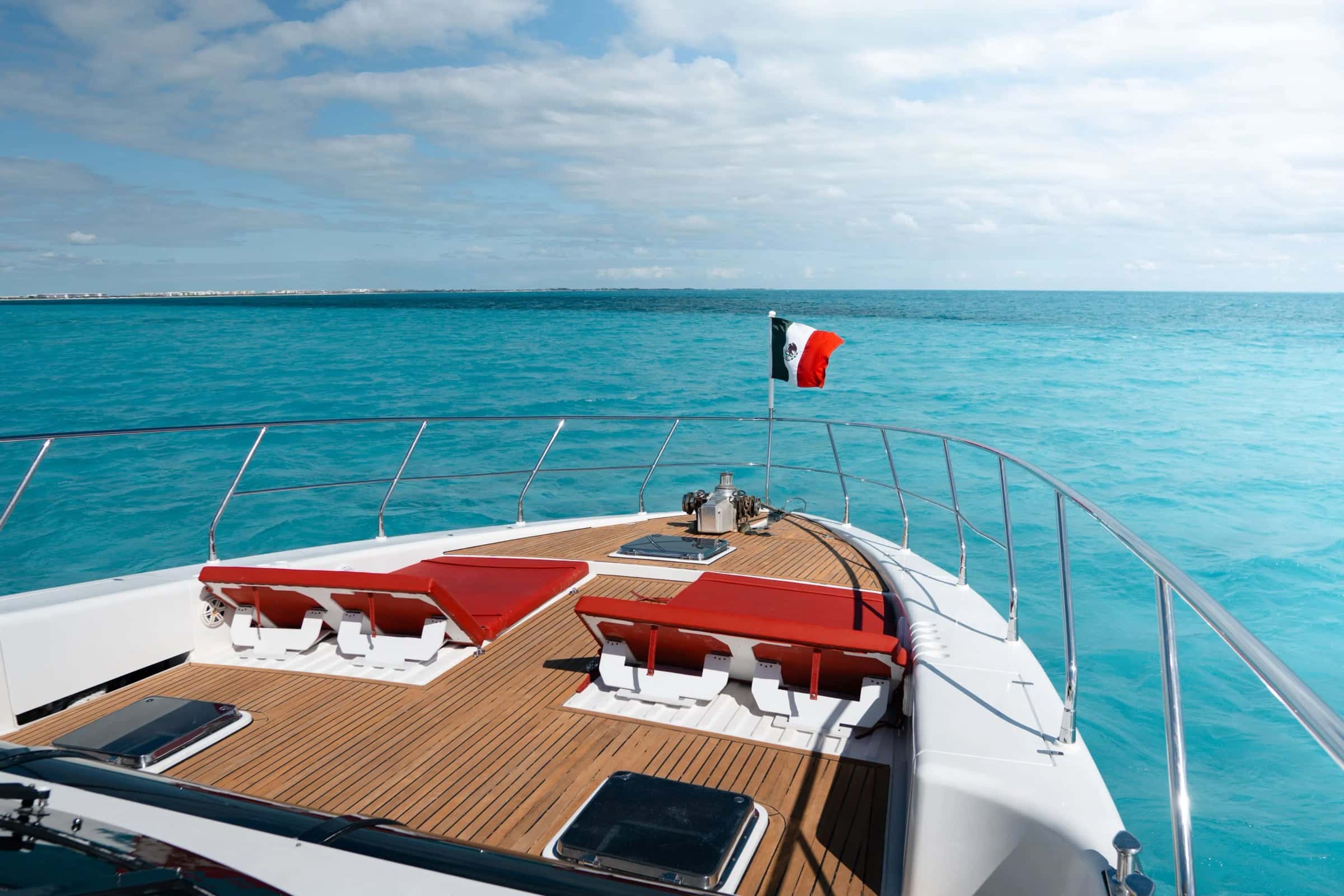 Red sunpads set into the teak foredeck, with the Mexican flag at the bow and open sea ahead