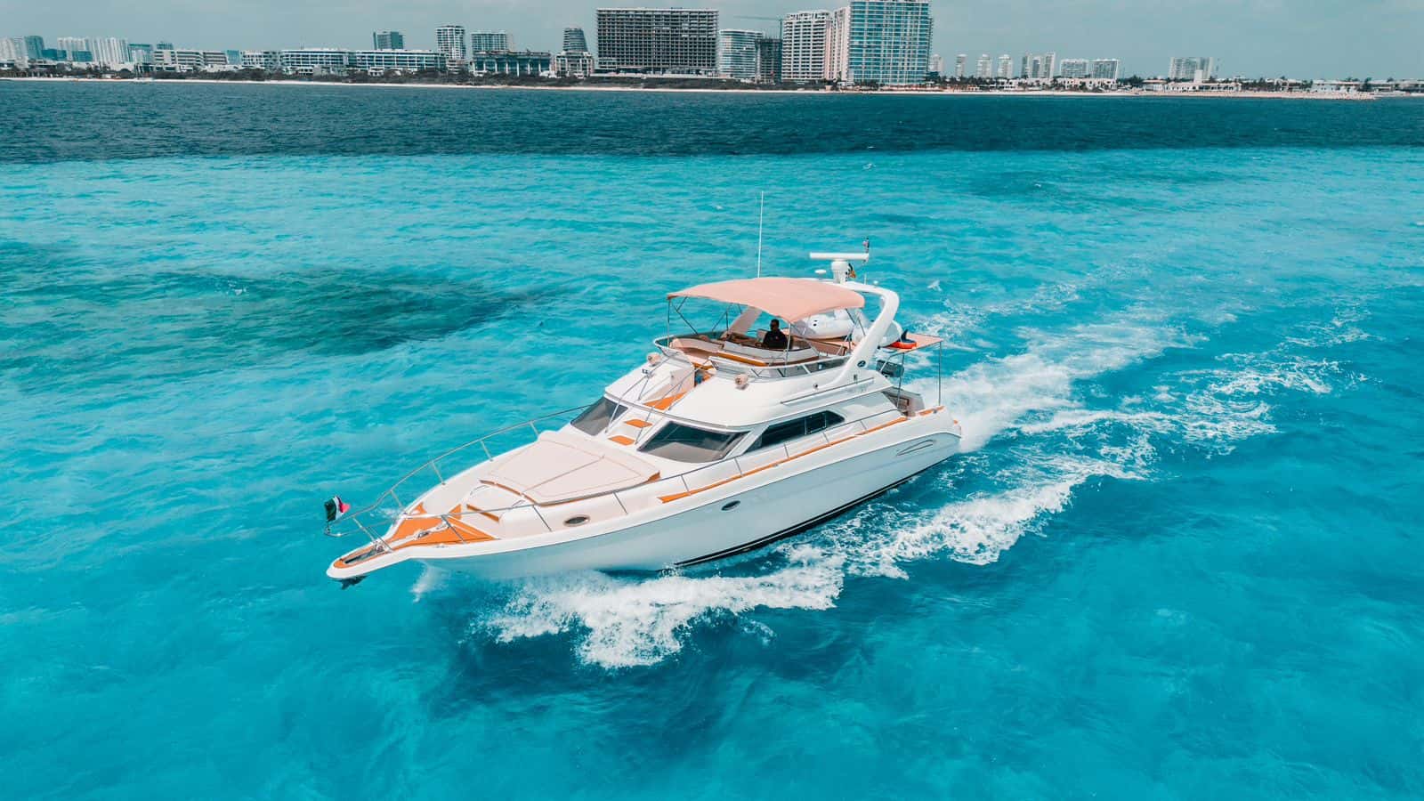 Mr Sea under way, bow quarter view with the flybridge and bimini and the Cancun hotel zone behind