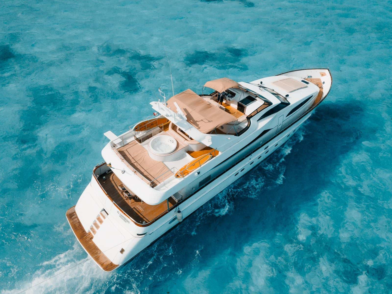 Aerial view of the yacht under way from the stern quarter, showing the Jacuzzi deck, flybridge and bow on turquoise water