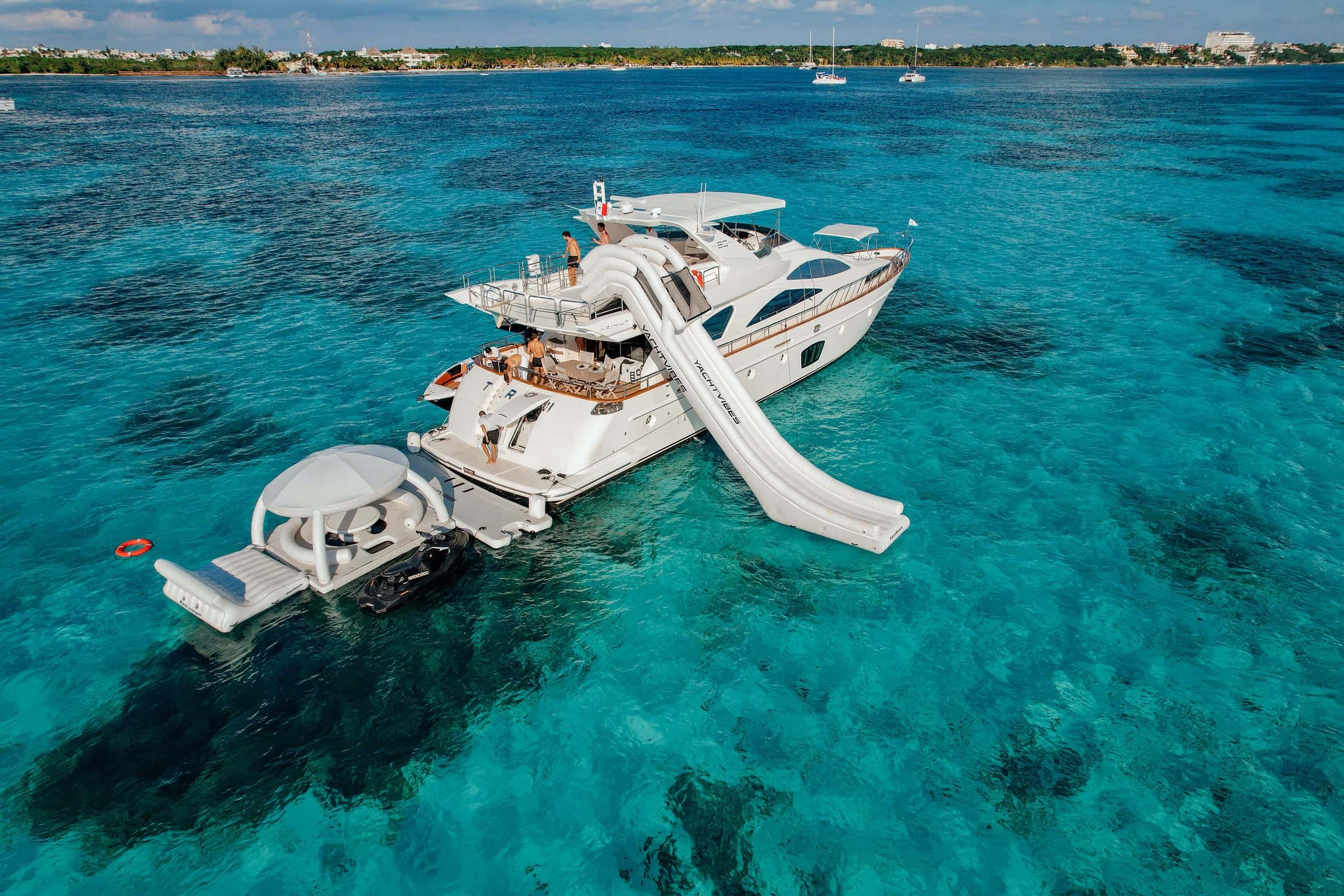 The yacht at anchor over a reef from the air, an inflatable slide off the side and a domed floating platform astern