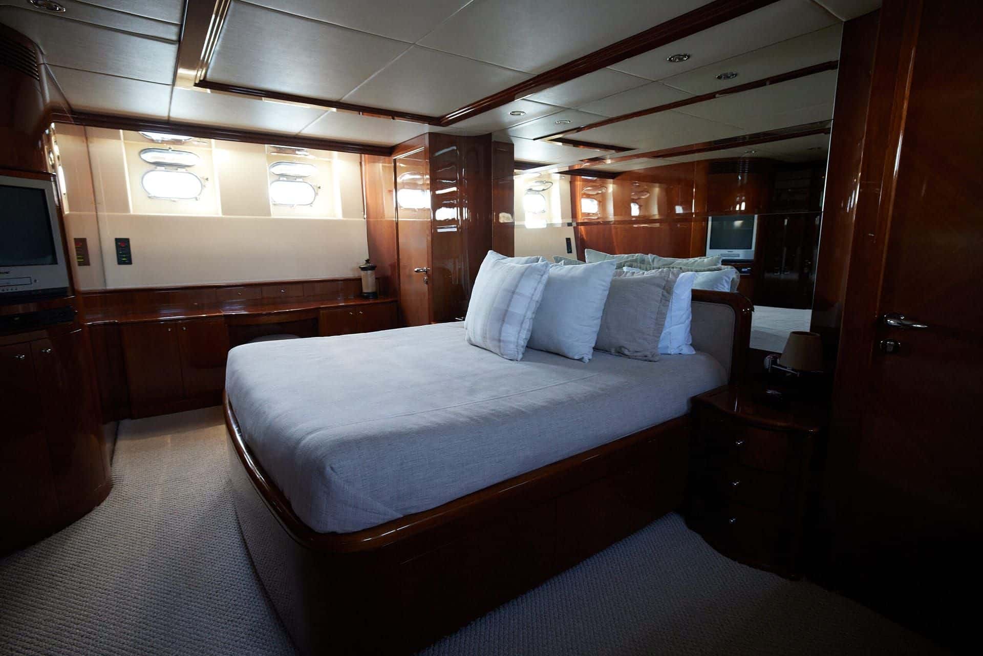 Guest stateroom with a double bed under portholes and a television on the wood cabinet