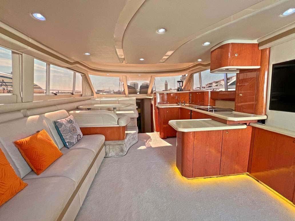 Saloon with a cream sofa and orange cushions facing the galley island, cherry cabinets lit from below