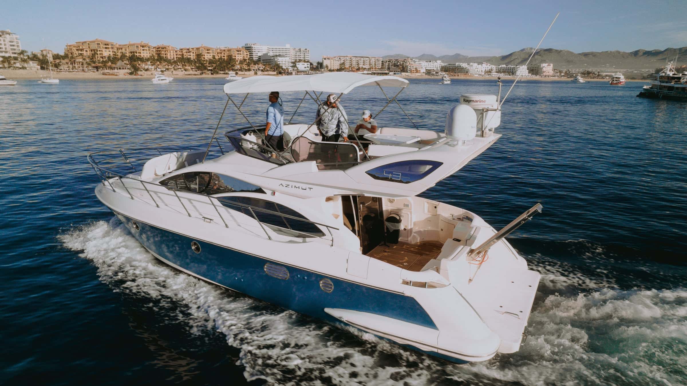 Golden under way off a hotel-lined beach, guests at the flybridge helm under the bimini
