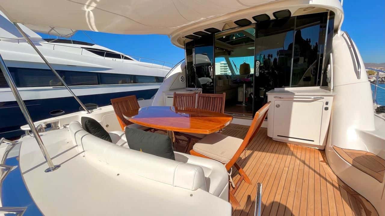 Cockpit with a teak table and wooden folding chairs on a teak deck, the sunroom doors behind