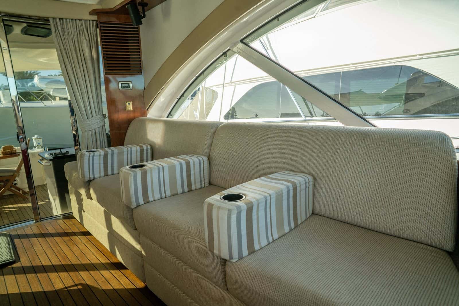 The sunroom's cream settee with striped cushions under curved windows, the teak sole and glass doors to the cockpit beside it