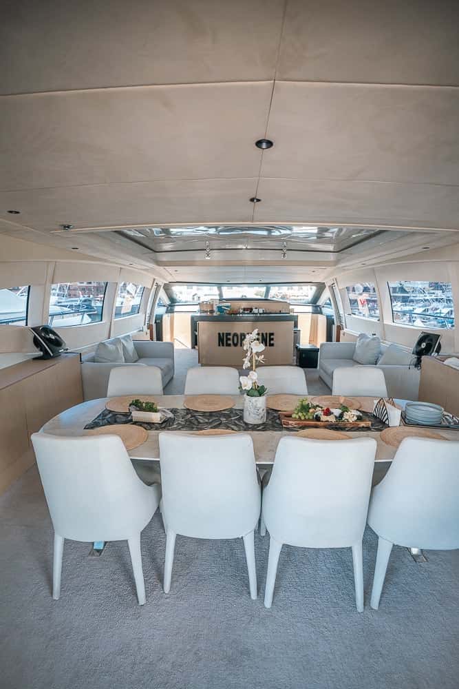 Saloon dining table laid for ten with white chairs, the lounge and a skylight beyond