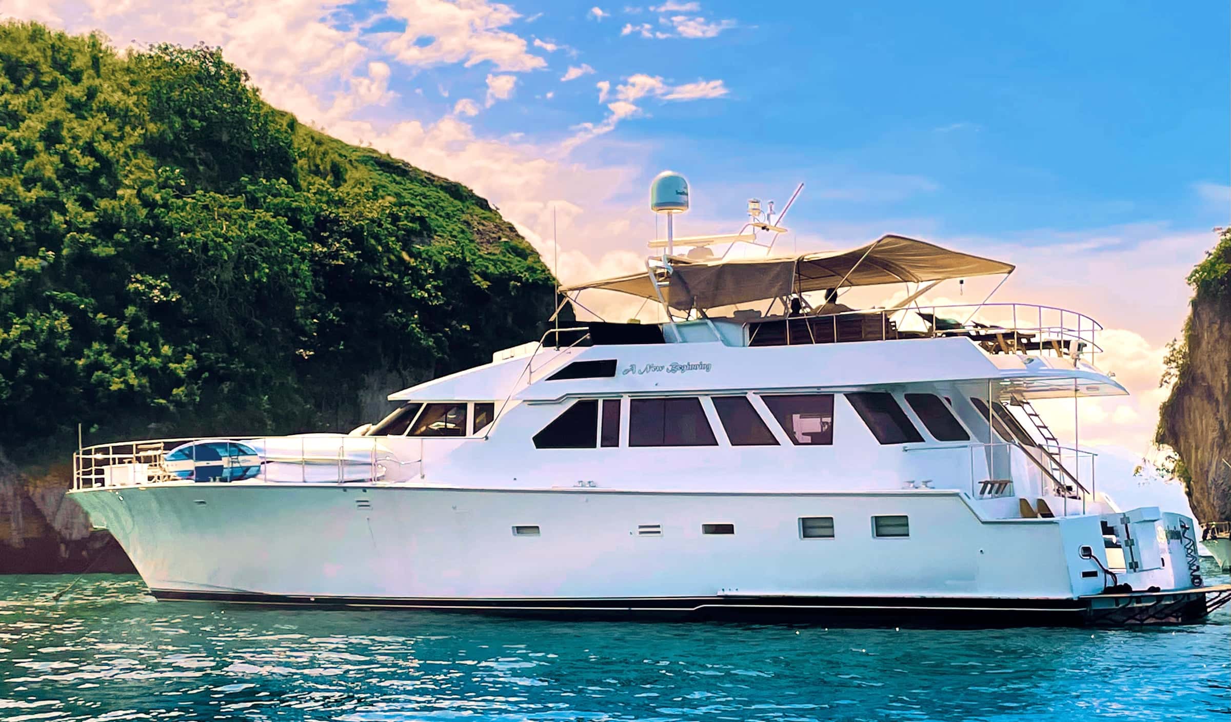 New Beginning, a white Cheoy Lee motor yacht with a flybridge, at anchor beside green rocky islets on clear water