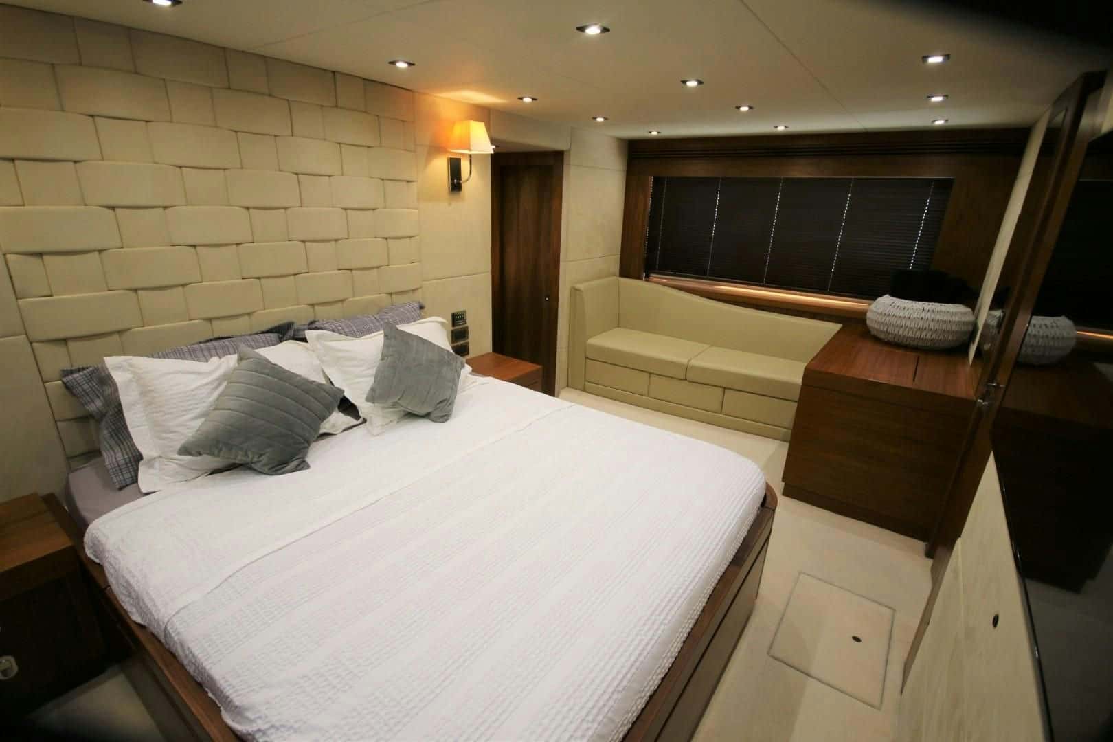 Double cabin with a padded wall, white bed cover and a sofa under the window