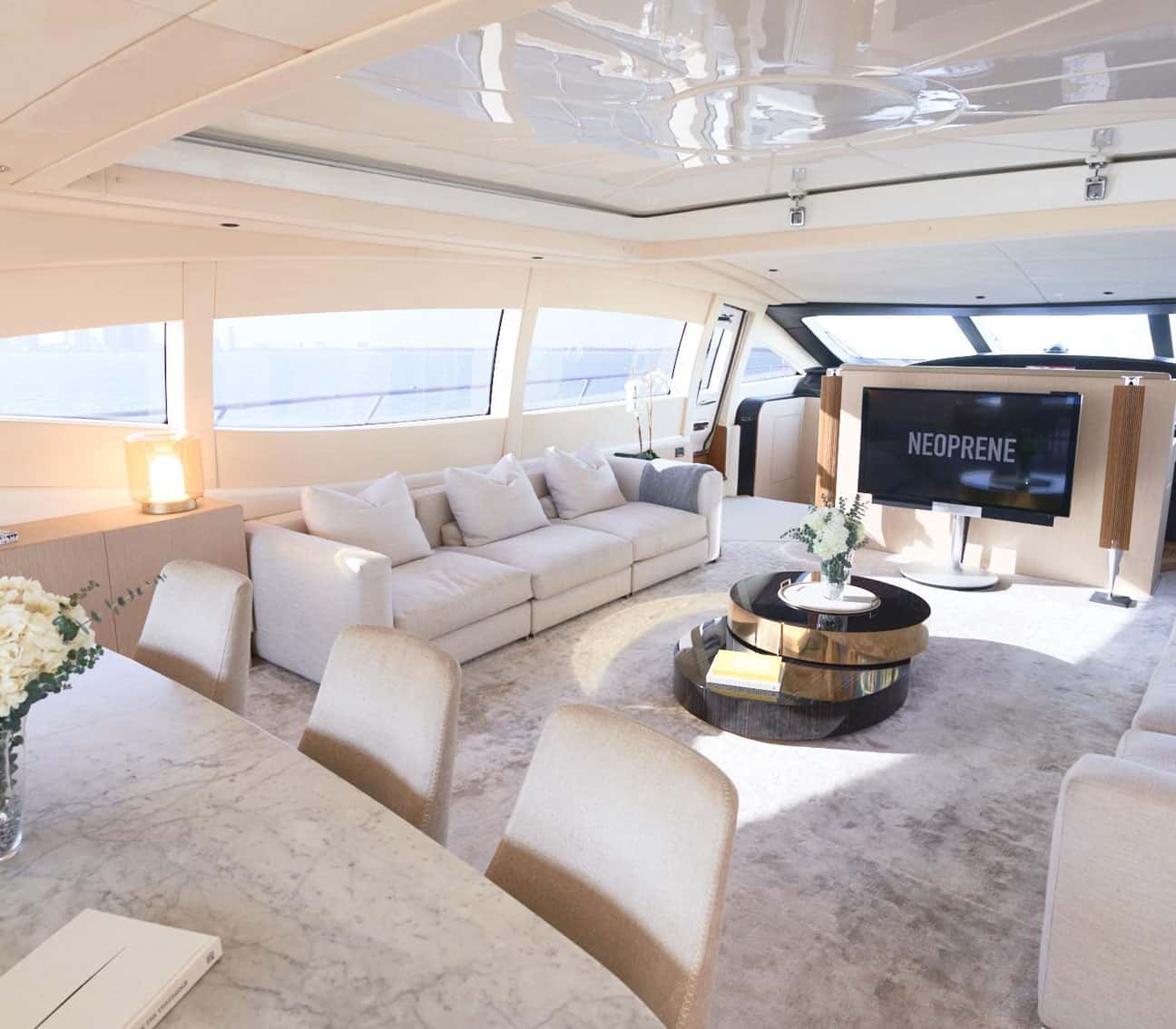 Bright saloon with a cream sofa, dining table with chairs, round coffee table and a TV