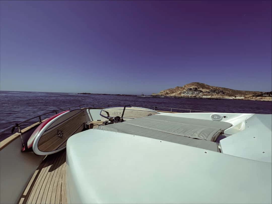 Bow with a cushioned sunpad and paddleboards stowed along the rail