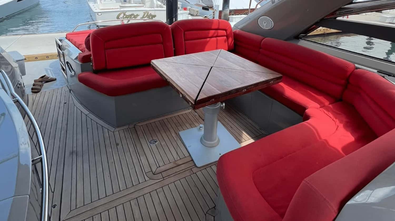 Cockpit with a U-shaped red settee, teak-topped table and teak-trimmed deck, moored in a marina