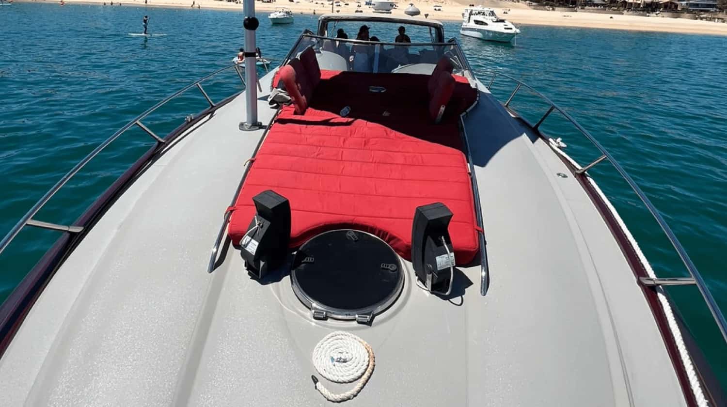 Red cushioned sunbathing pad on the bow, seen from the foredeck with the bay and beach behind