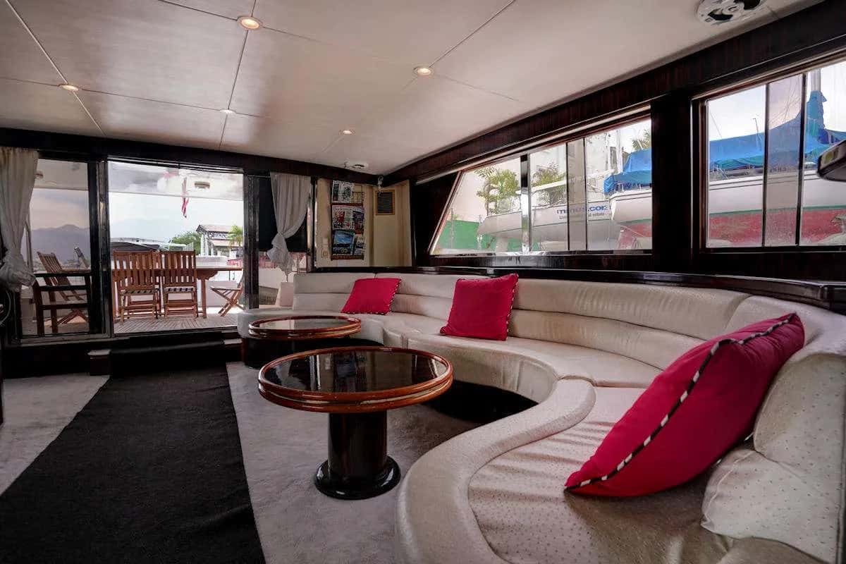 Saloon with a curved cream sofa, red cushions and view of the aft dining deck