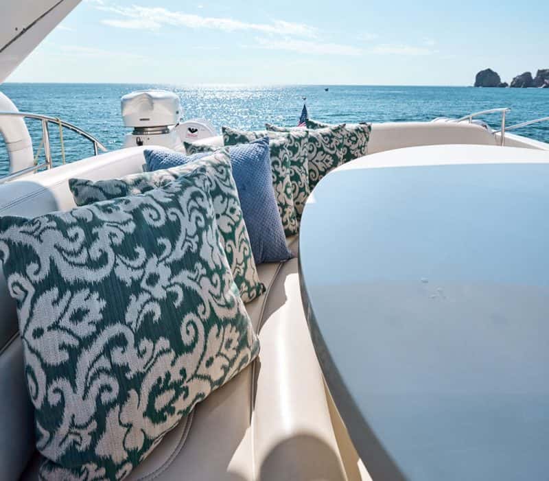 Patterned cushions on a curved cream bench beside a round table, with the sea and rocks behind