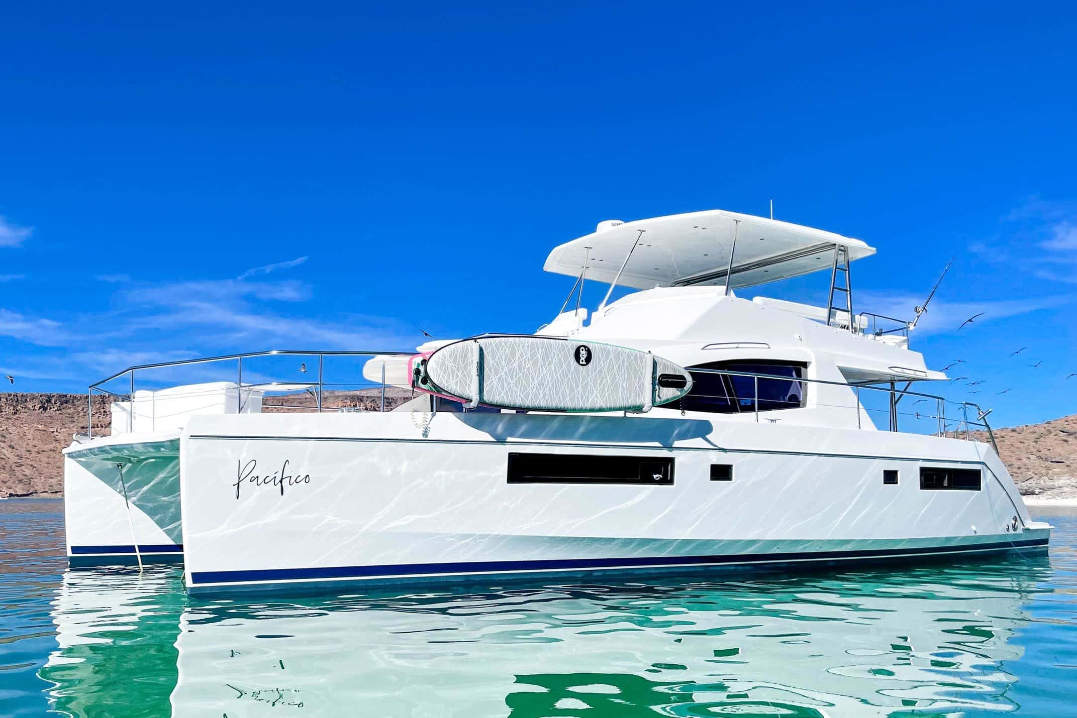 Side view of the catamaran Pacifico with a paddleboard on the rail, a flybridge hardtop and turquoise water