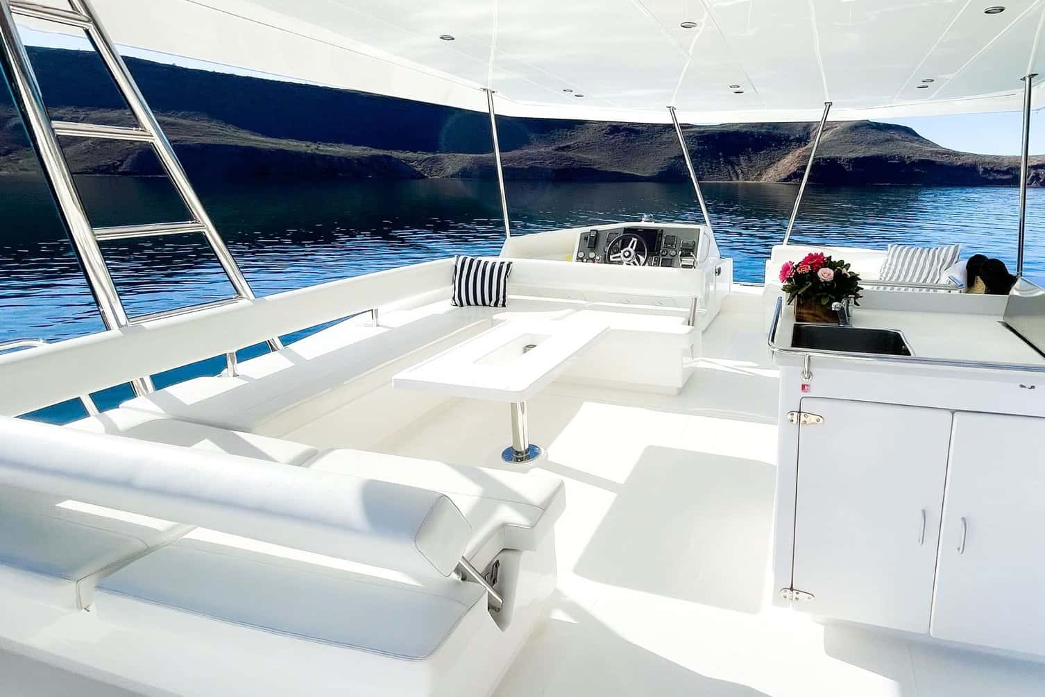 Flybridge with white cushioned seating, a table, the helm and a sink counter under a hardtop