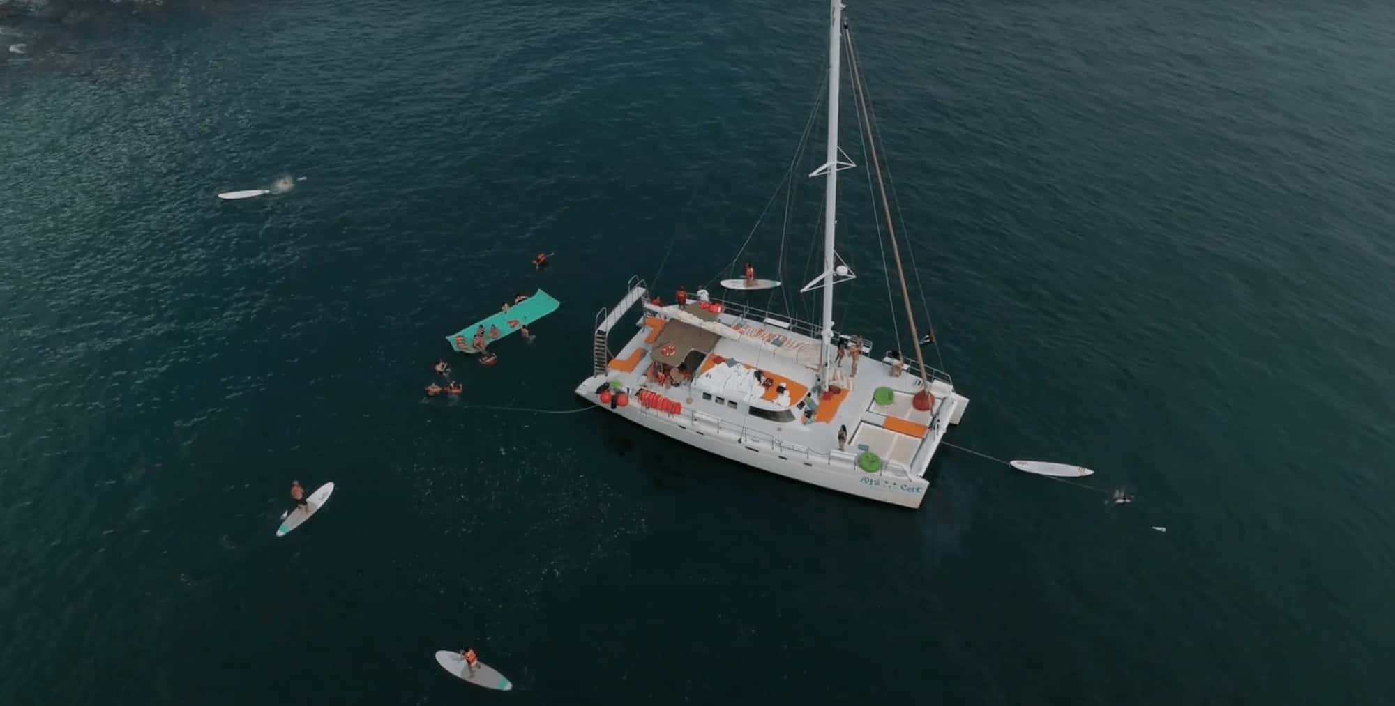 Ally Cat catamaran seen from above, with paddleboards, a floating mat and swimmers around it