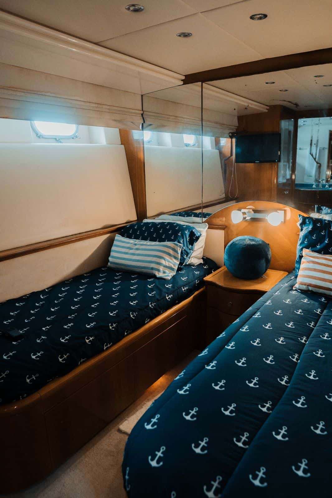 Twin cabin with two single beds in navy anchor-print bedding, portholes and a wall TV