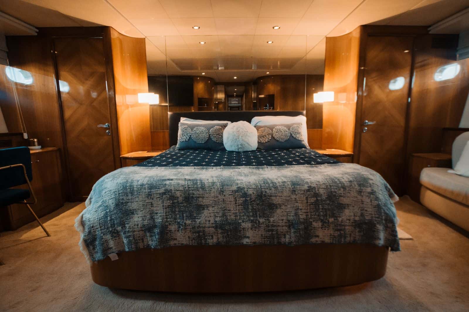 Master cabin with a large island bed in navy anchor bedding, mirrored headboard wall and wood panelling
