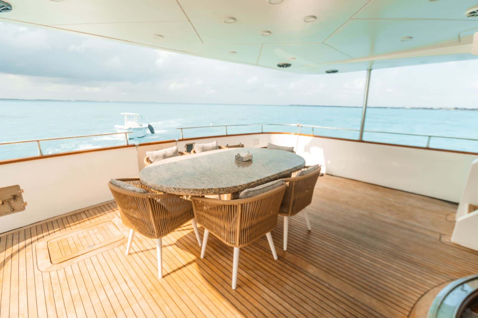 Covered aft deck with an oval stone-top dining table and six woven chairs on teak decking