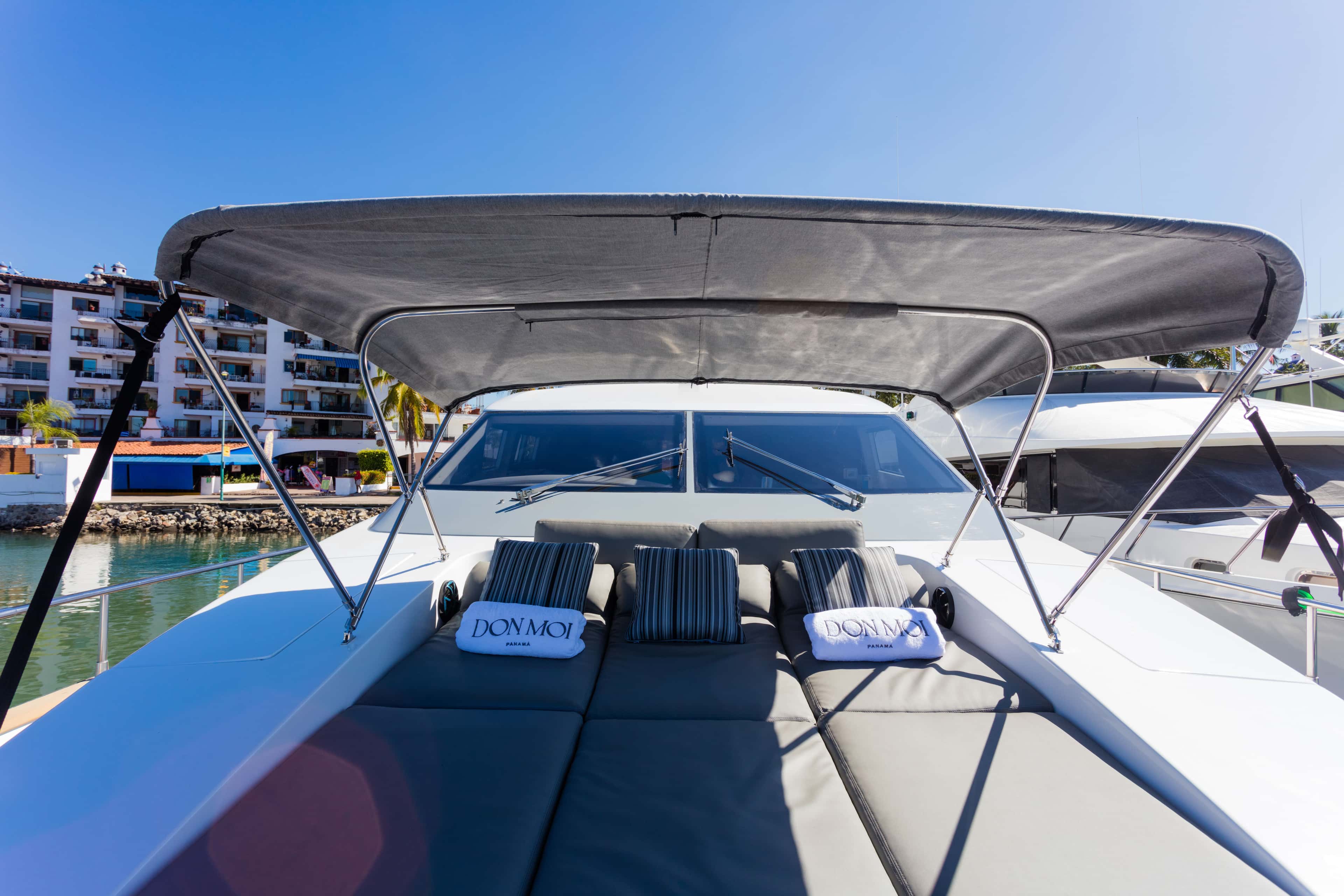 Foredeck sunbathing cushions under a grey bimini, with Don Moi towels