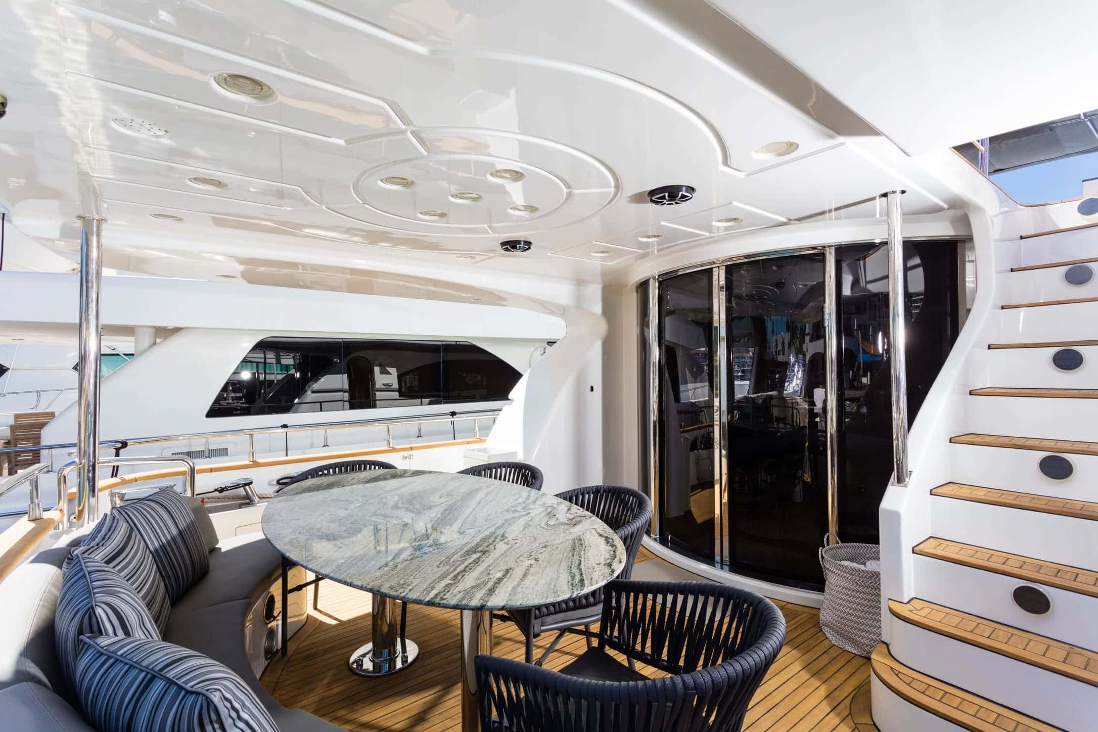 Covered aft deck with a stone dining table, chairs, a curved sofa, sliding glass doors and stairs