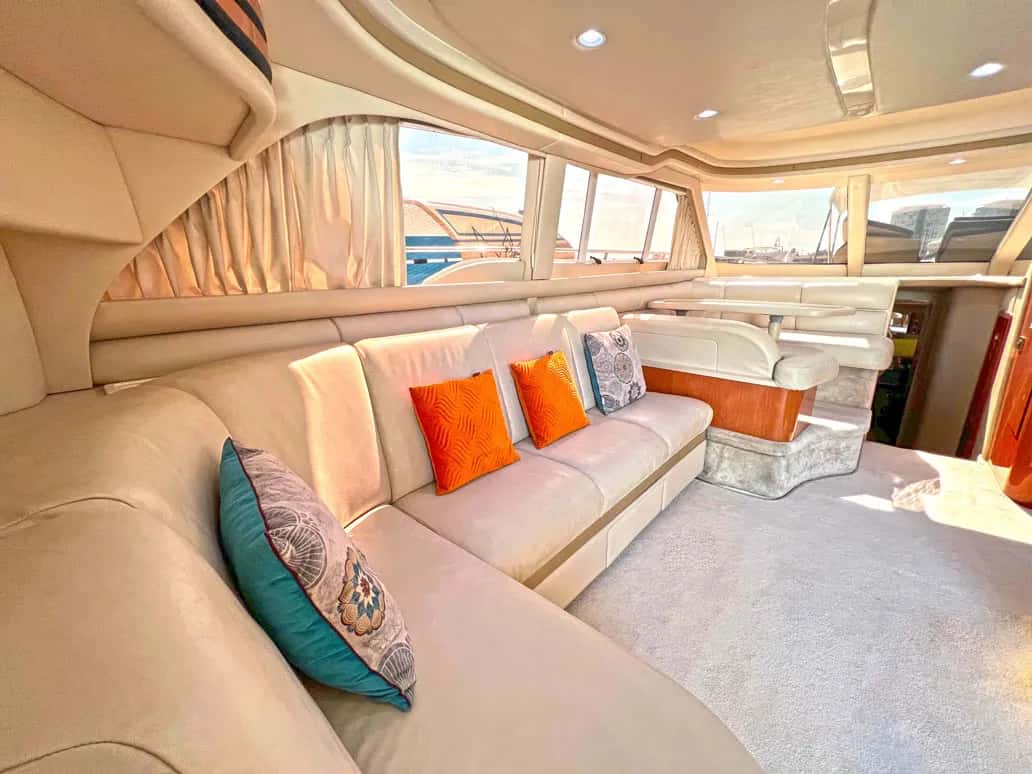 Saloon with a long cream sofa, orange cushions and a dinette beside large windows