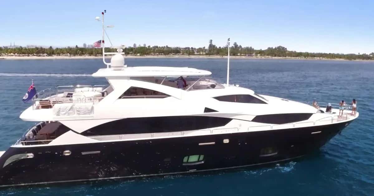 Yacht seen from the side at sea, dark hull and white superstructure, with guests on the foredeck