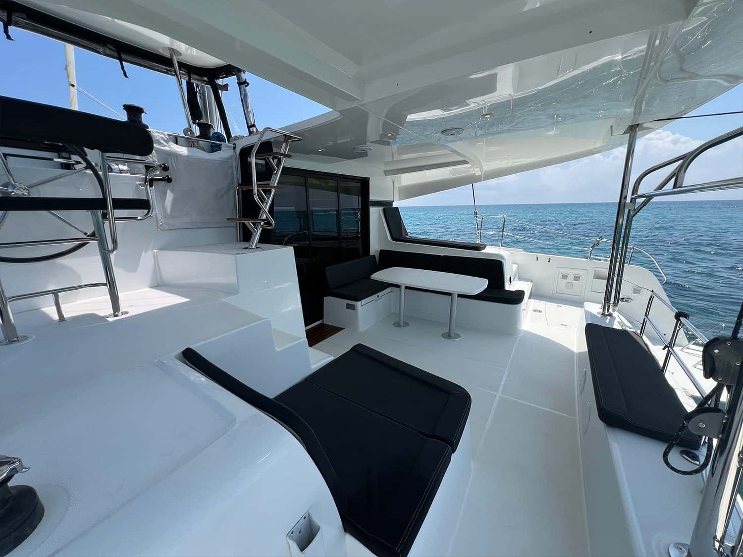 Shaded cockpit with dining table, black cushioned benches and steps to the helm