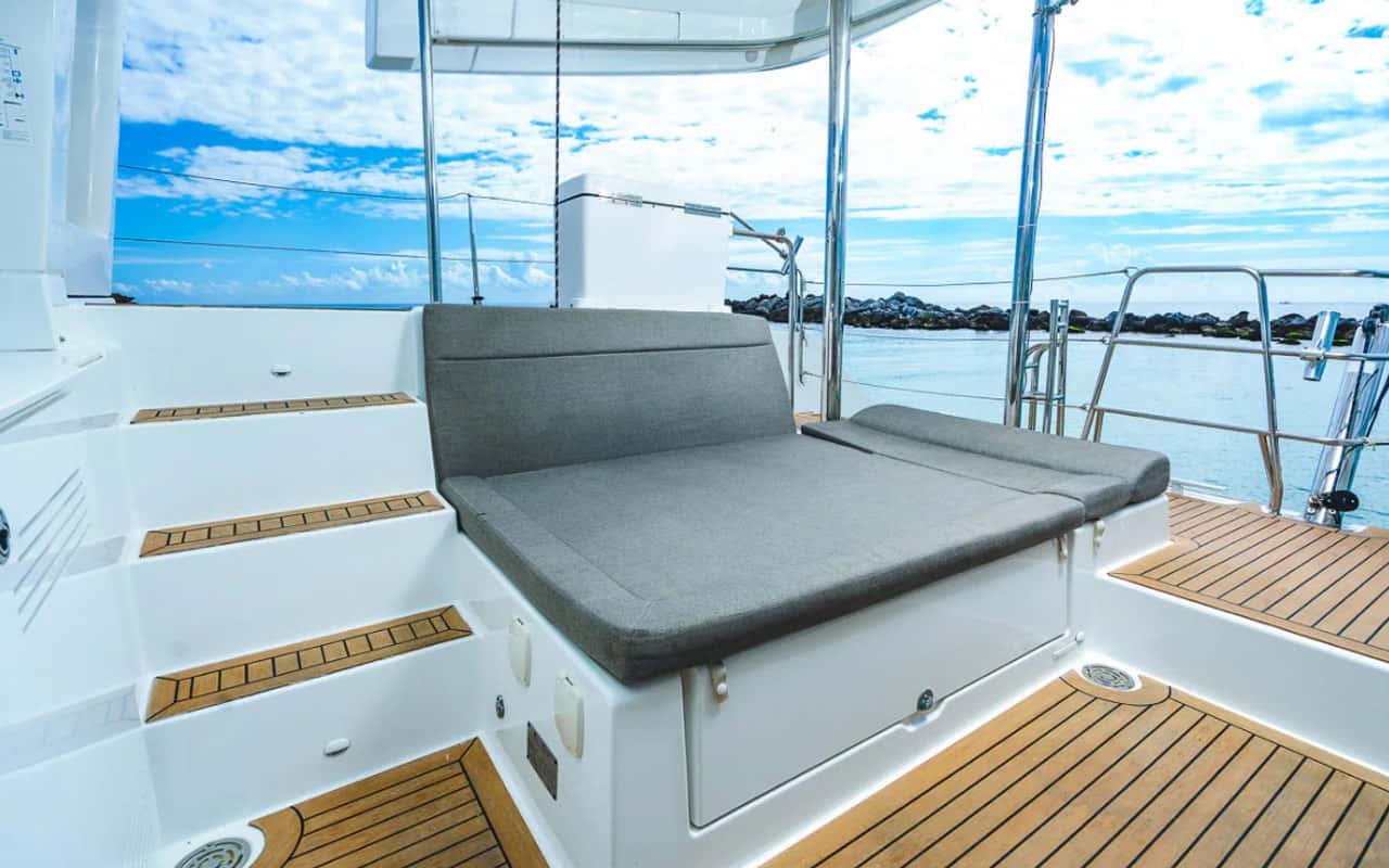 Grey cushioned sunbed at the stern beside teak steps
