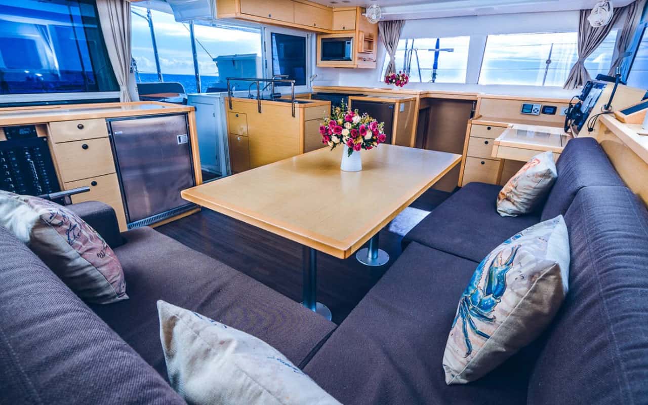 Saloon with dining table, dark sofas and galley behind